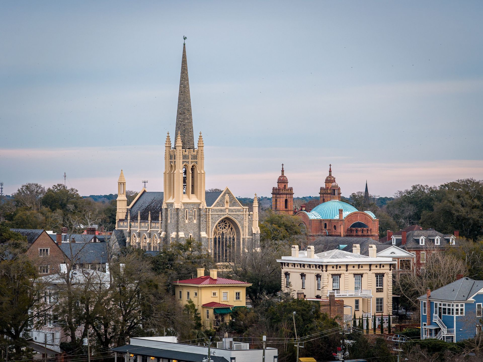 City skyline with a tall Gothic church spire above historic buildings under a cloudy sky