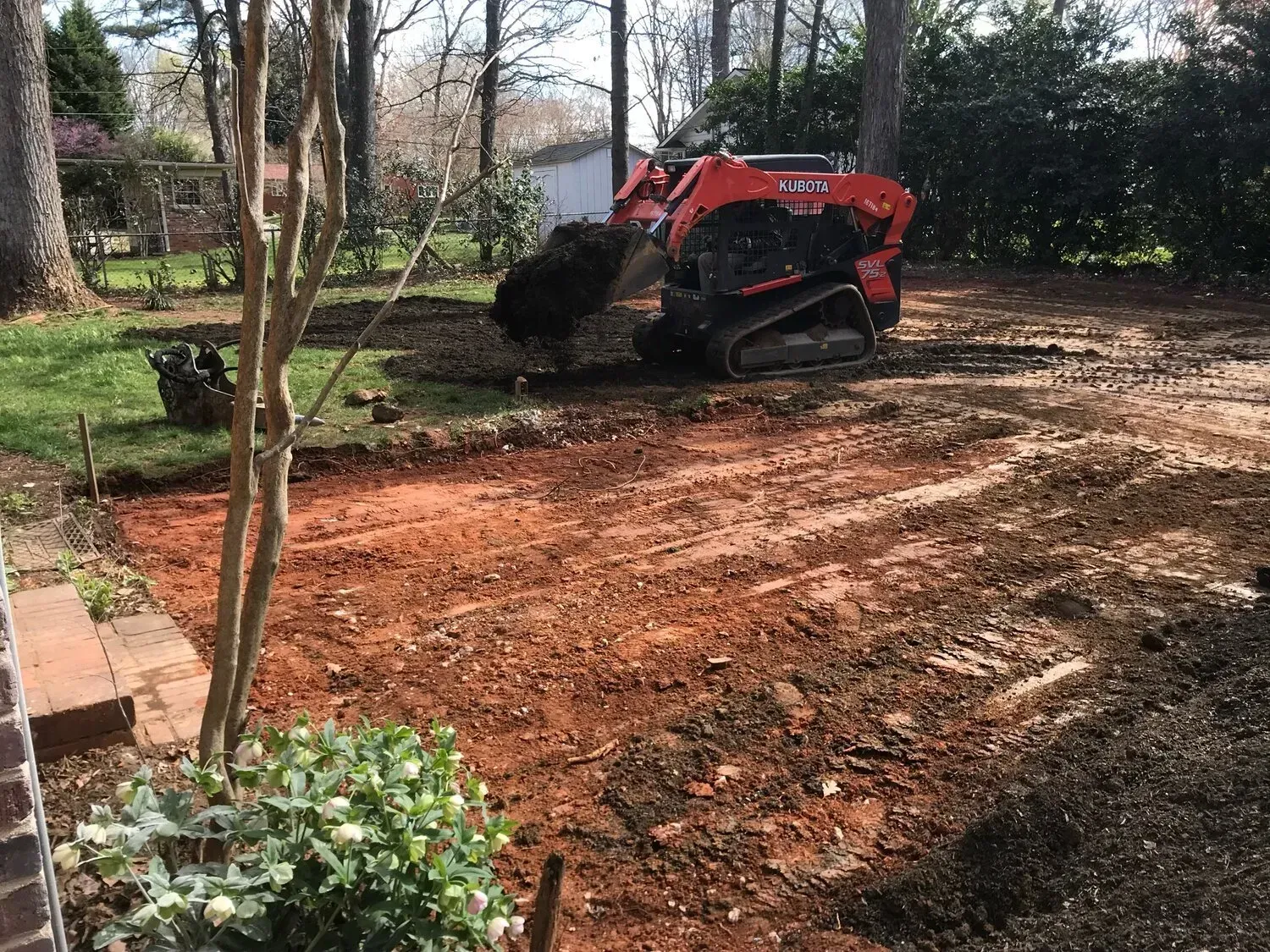 A red skid-steer loader clears dirt and landscape debris from a residential backyard.