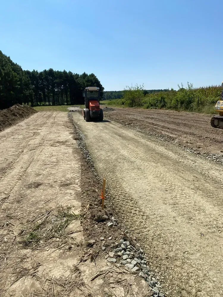 An orange tractor driving on a gravel road through a construction site under a clear blue sky.
