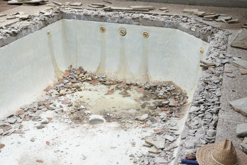 An empty, rectangular swimming pool undergoing renovation with construction debris on the floor and edges.