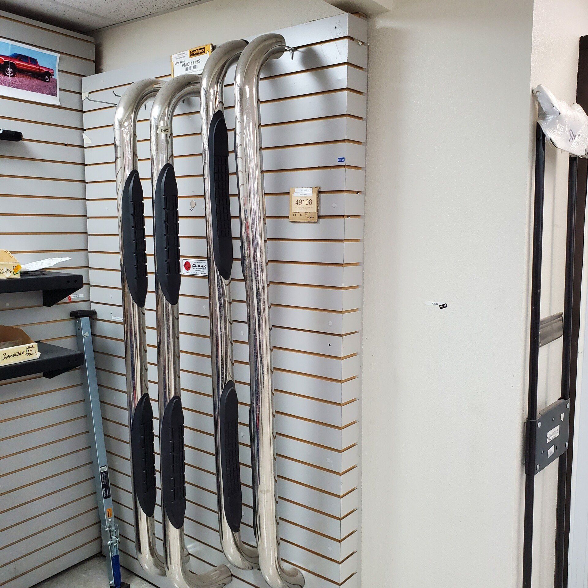 Four silver truck running boards displayed on a slatted wall.