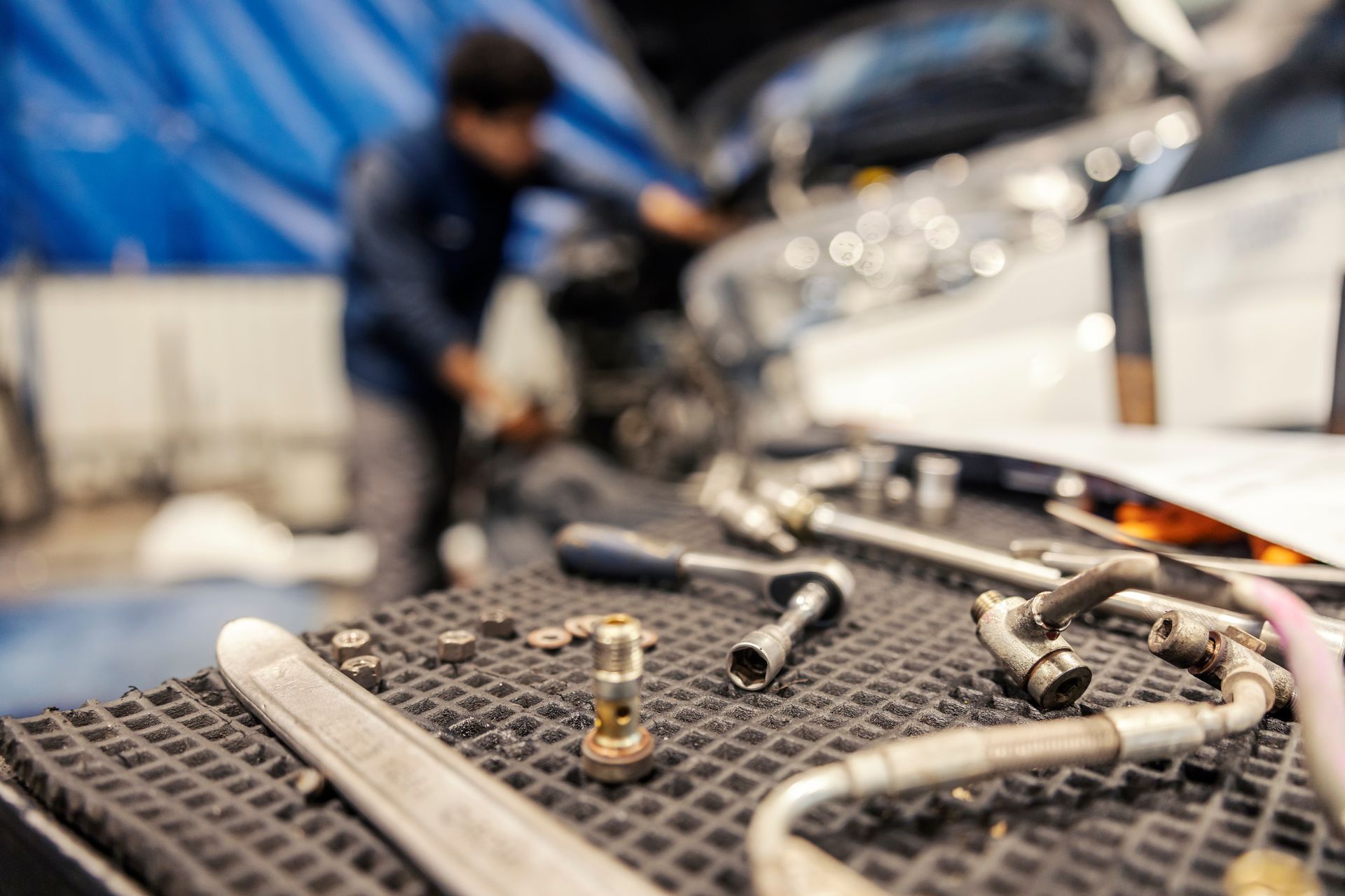 Truck equipment technician working in a shop with hand tools and hydraulic fittings on a workbench Auto repair tools on a workbench with a mechanic and car in the background