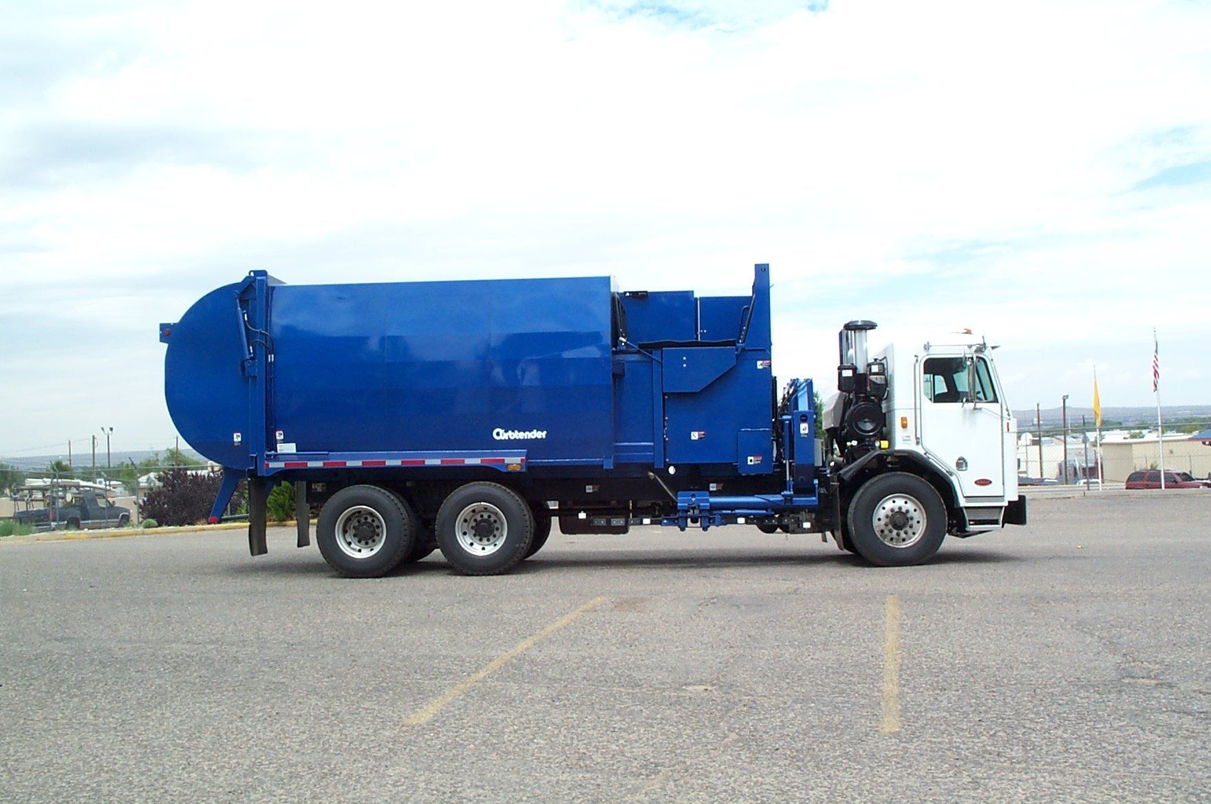 Blue and white garbage truck parked in a parking lot on a cloudy day.