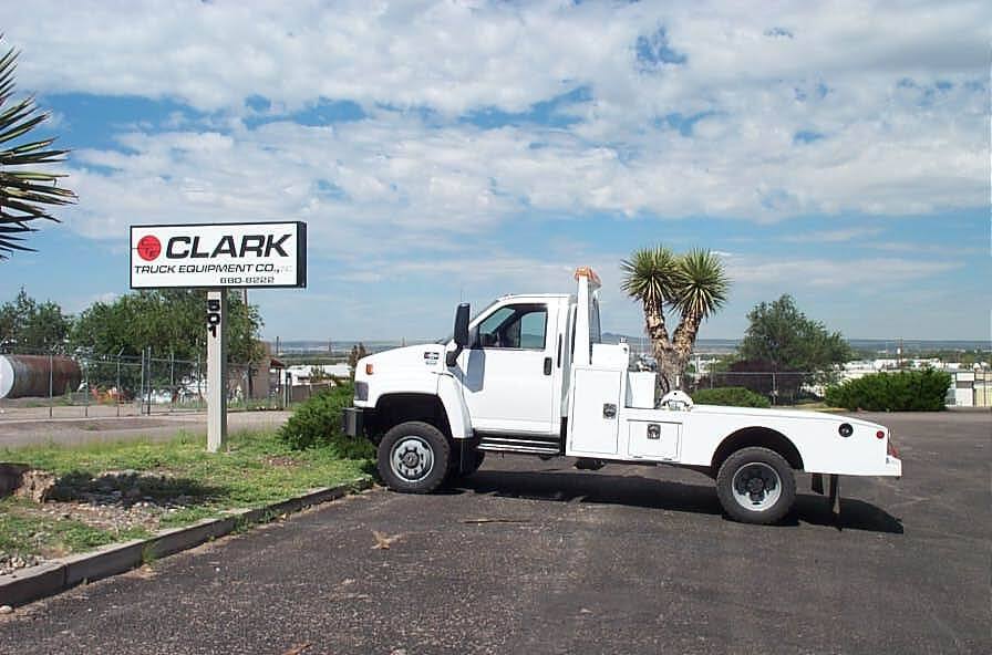 White service truck parked near a sign for Clark Truck and Equipment. Blue sky, brown asphalt.