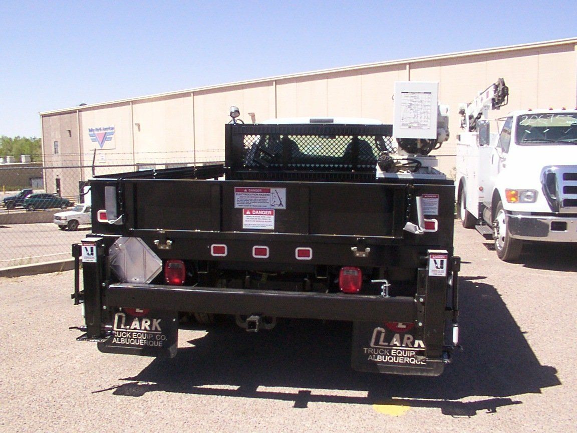 Black truck bed with warning signs, license plate, and lights, parked outdoors.