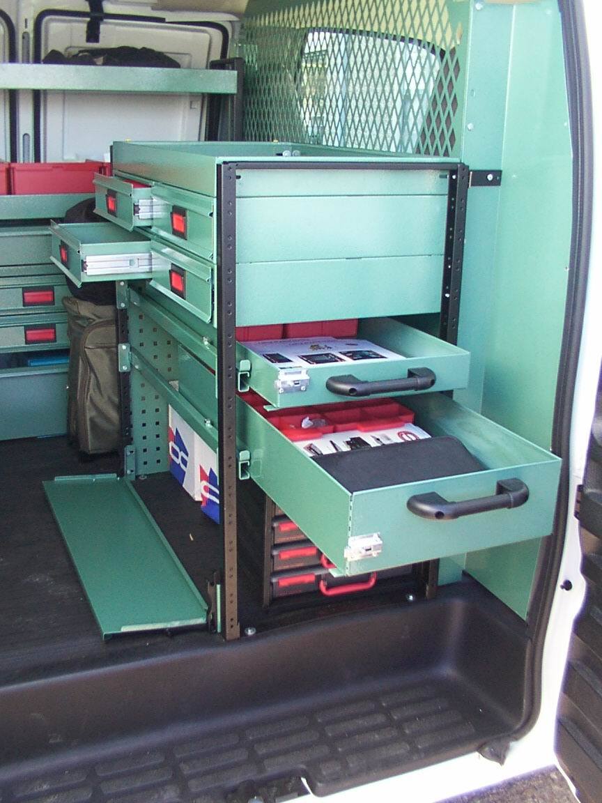Green metal tool storage drawers in a van, some drawers open, containing tools and supplies.