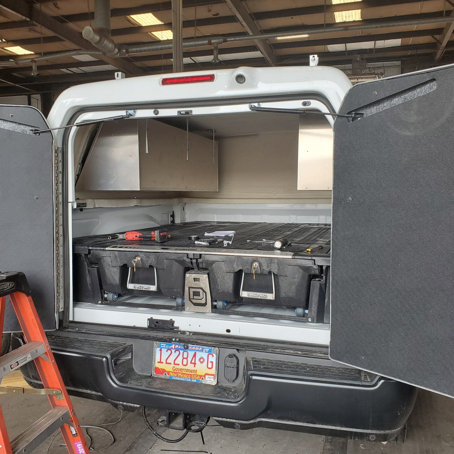 White truck bed with drawers and storage under a canopy. A ladder stands to the side.