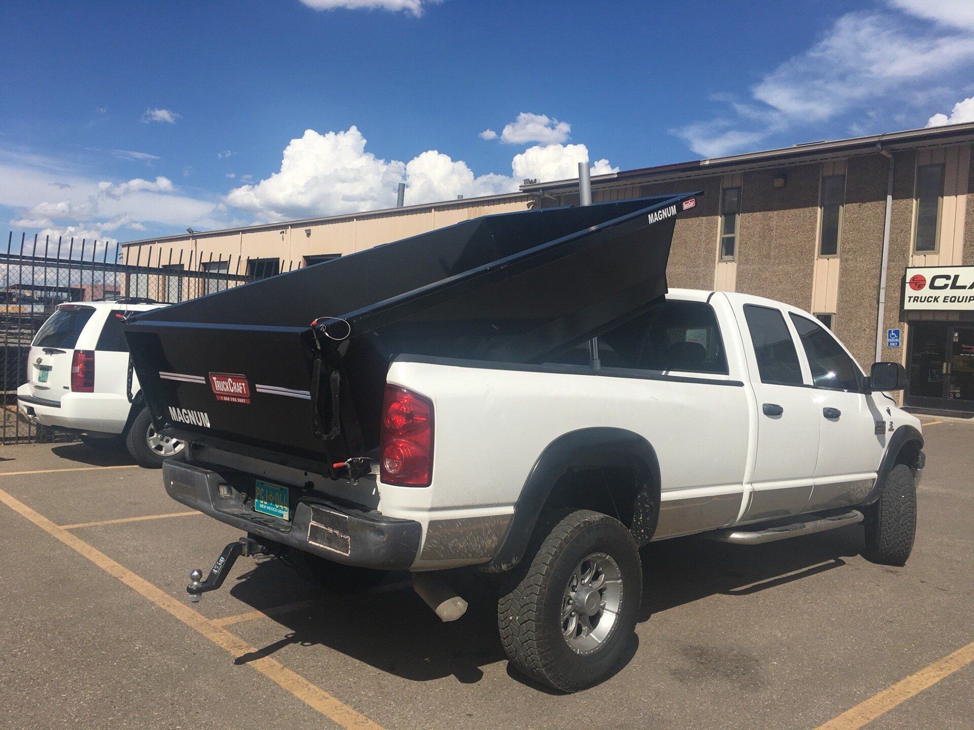 White pickup truck with a black dump bed raised in a parking lot.
