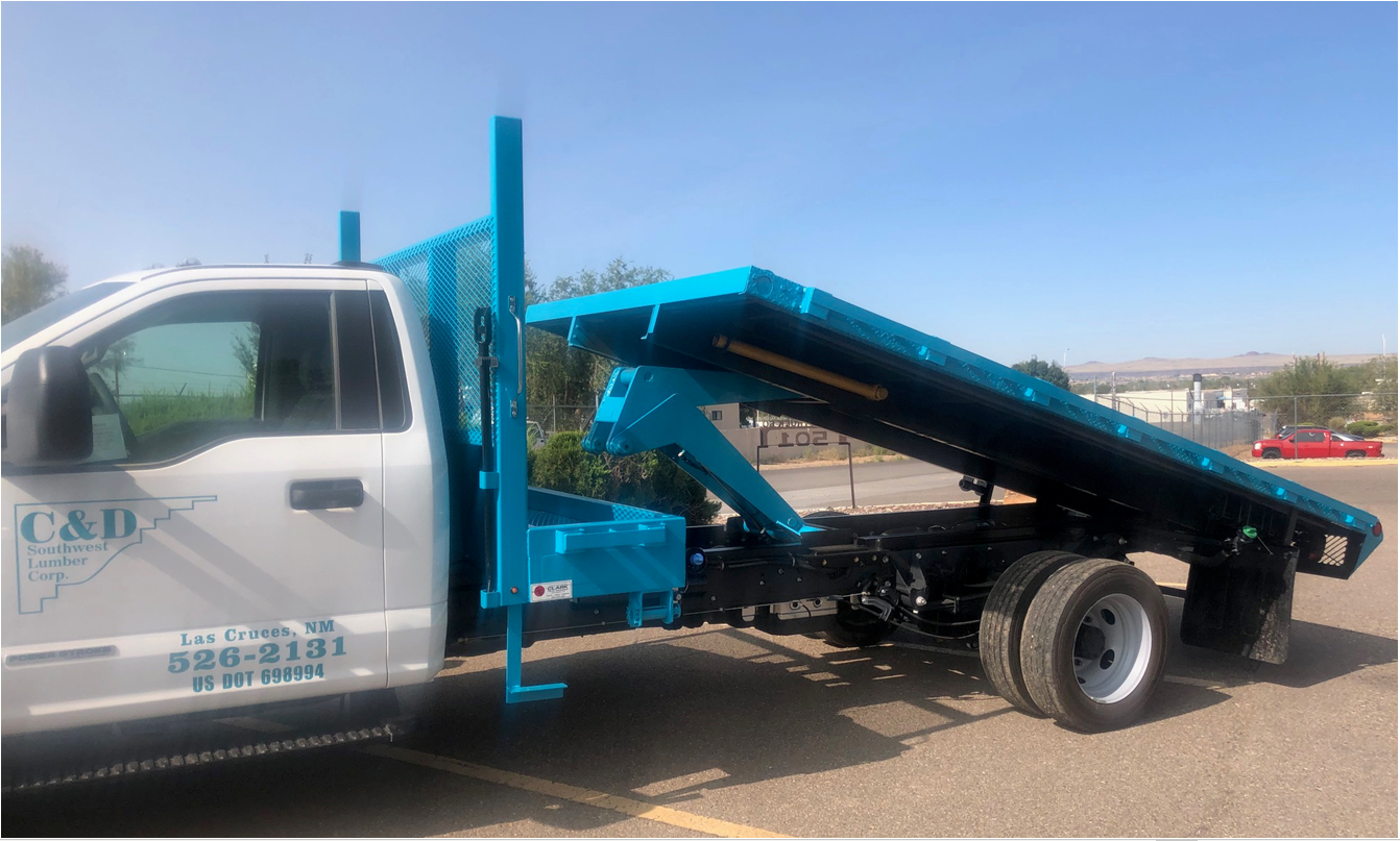 White truck with a blue flatbed in a parking lot on a sunny day. The bed is raised.