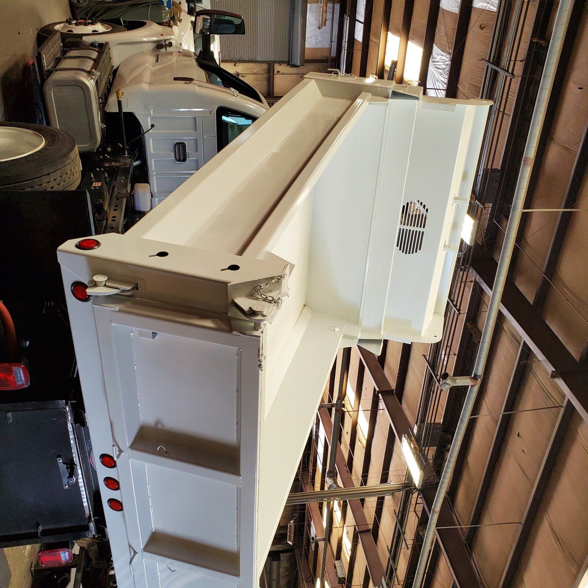 White dump truck bed, angled view, against a warehouse wall.