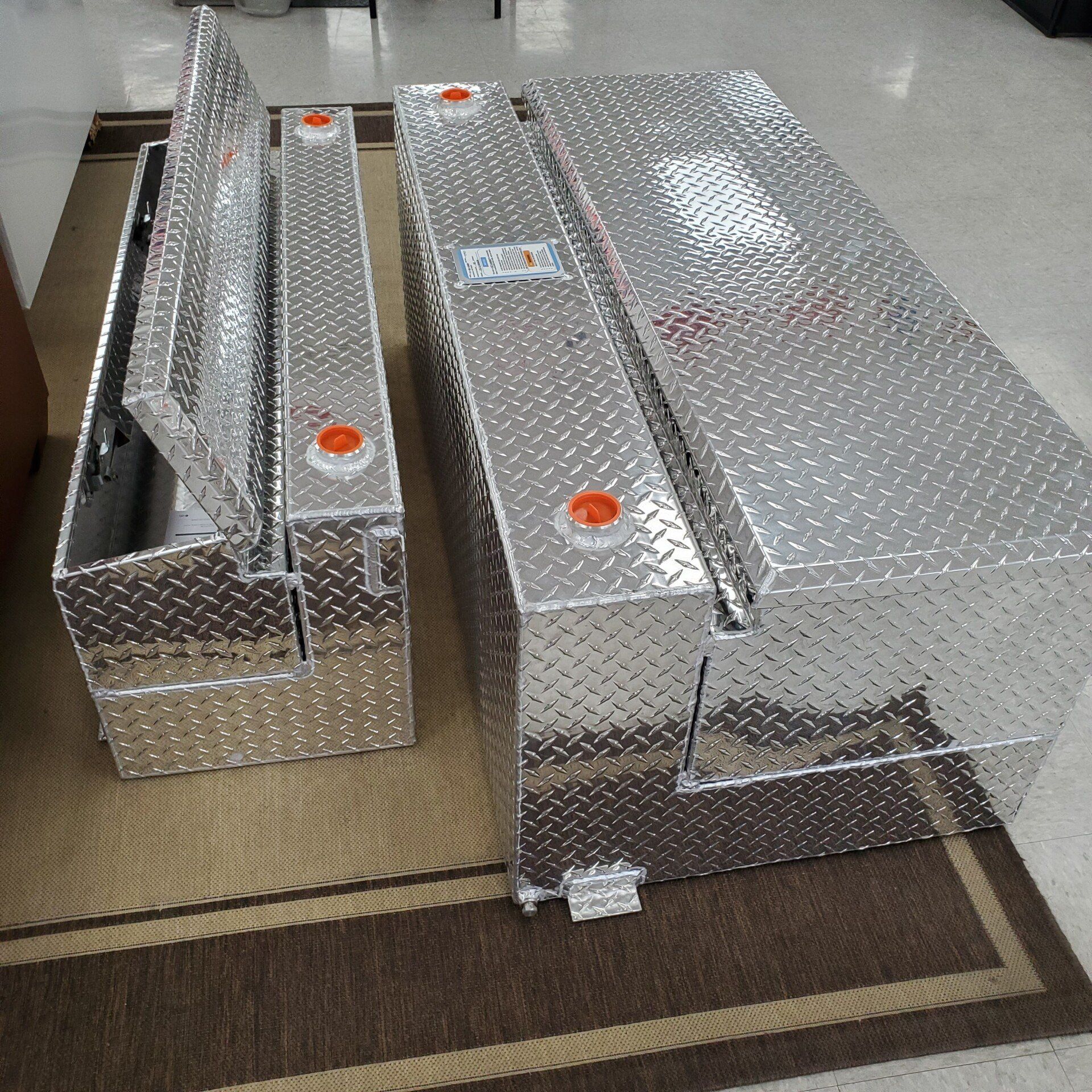 Three shiny aluminum truck toolboxes on a rug. Two have lids open.