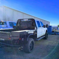 White and black pickup truck with a flatbed, parked outdoors under a blue sky.