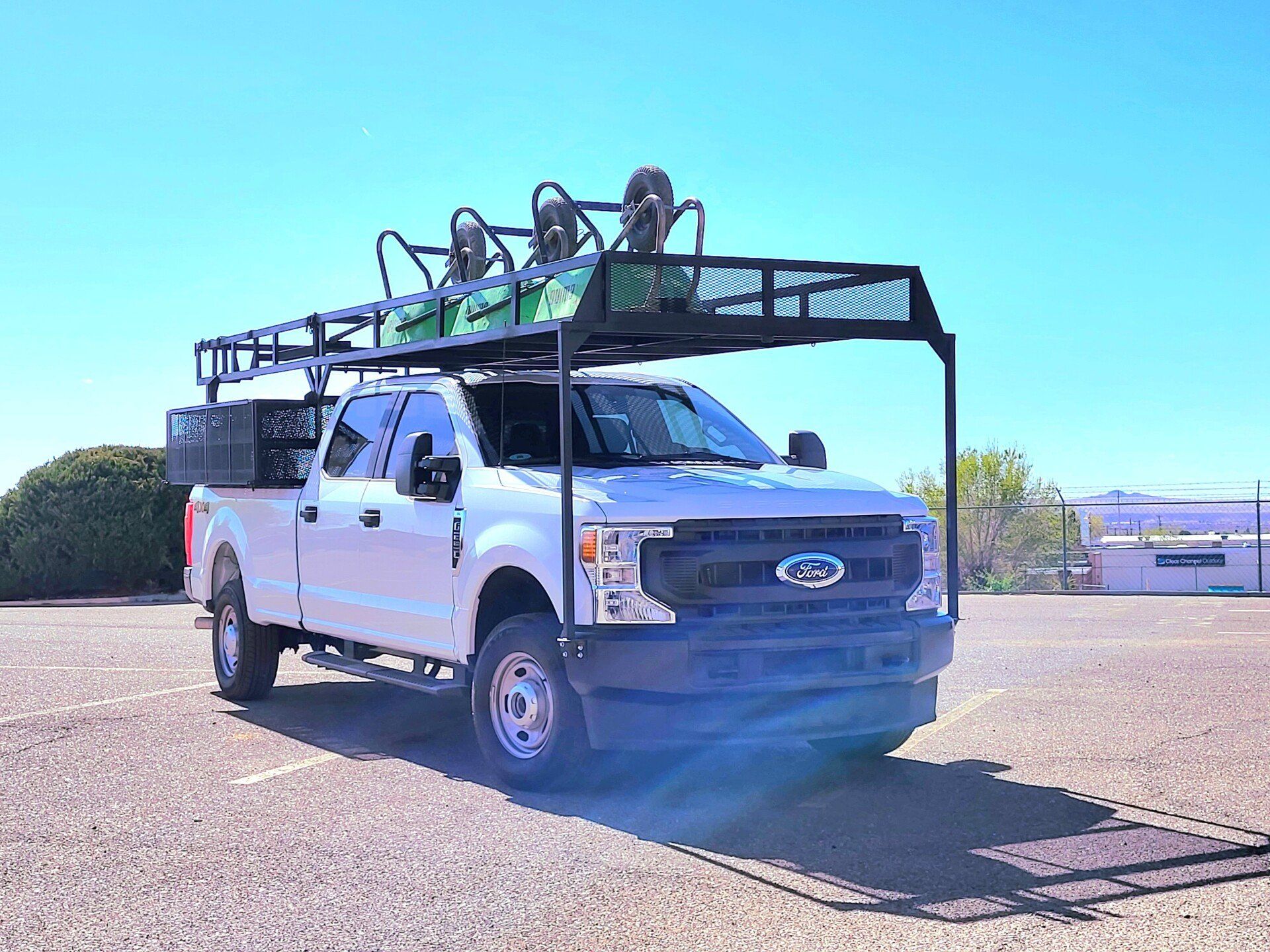 White truck with equipment rack on top, parked in a lot on a sunny day.