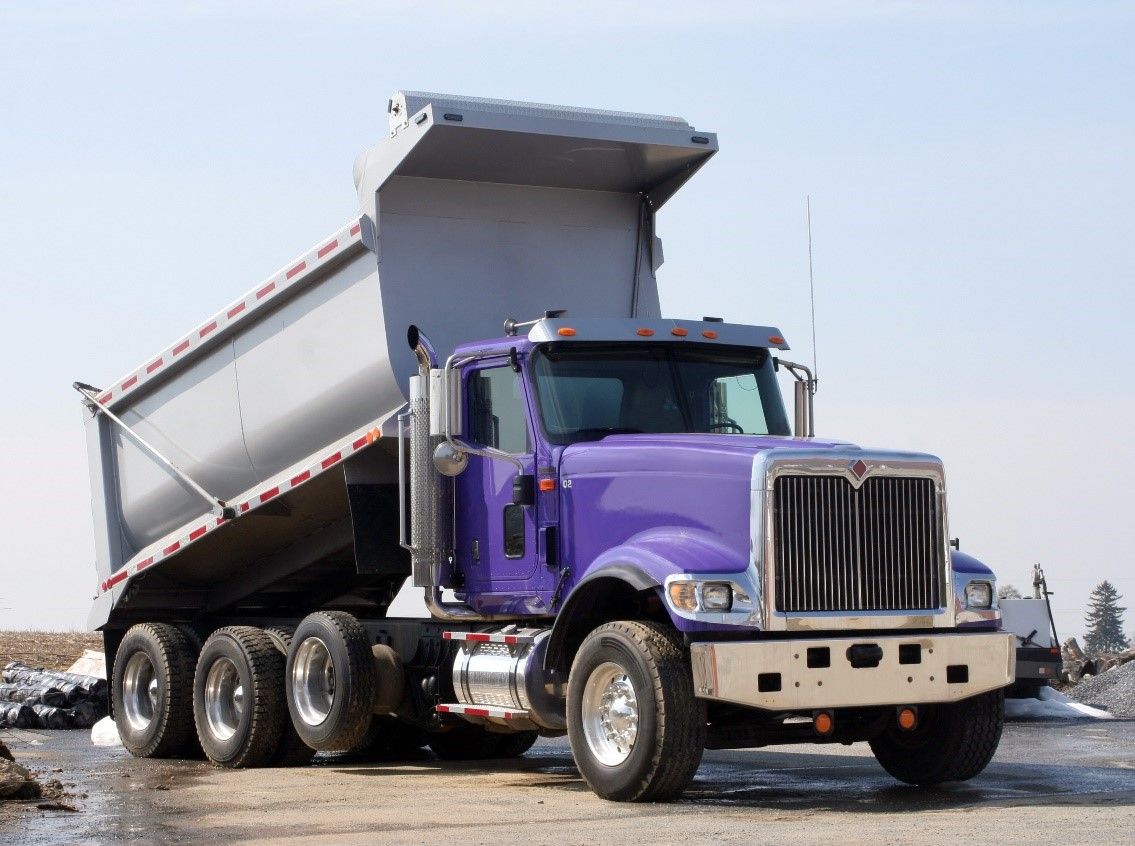 Purple dump truck with raised bed, parked on a paved area.