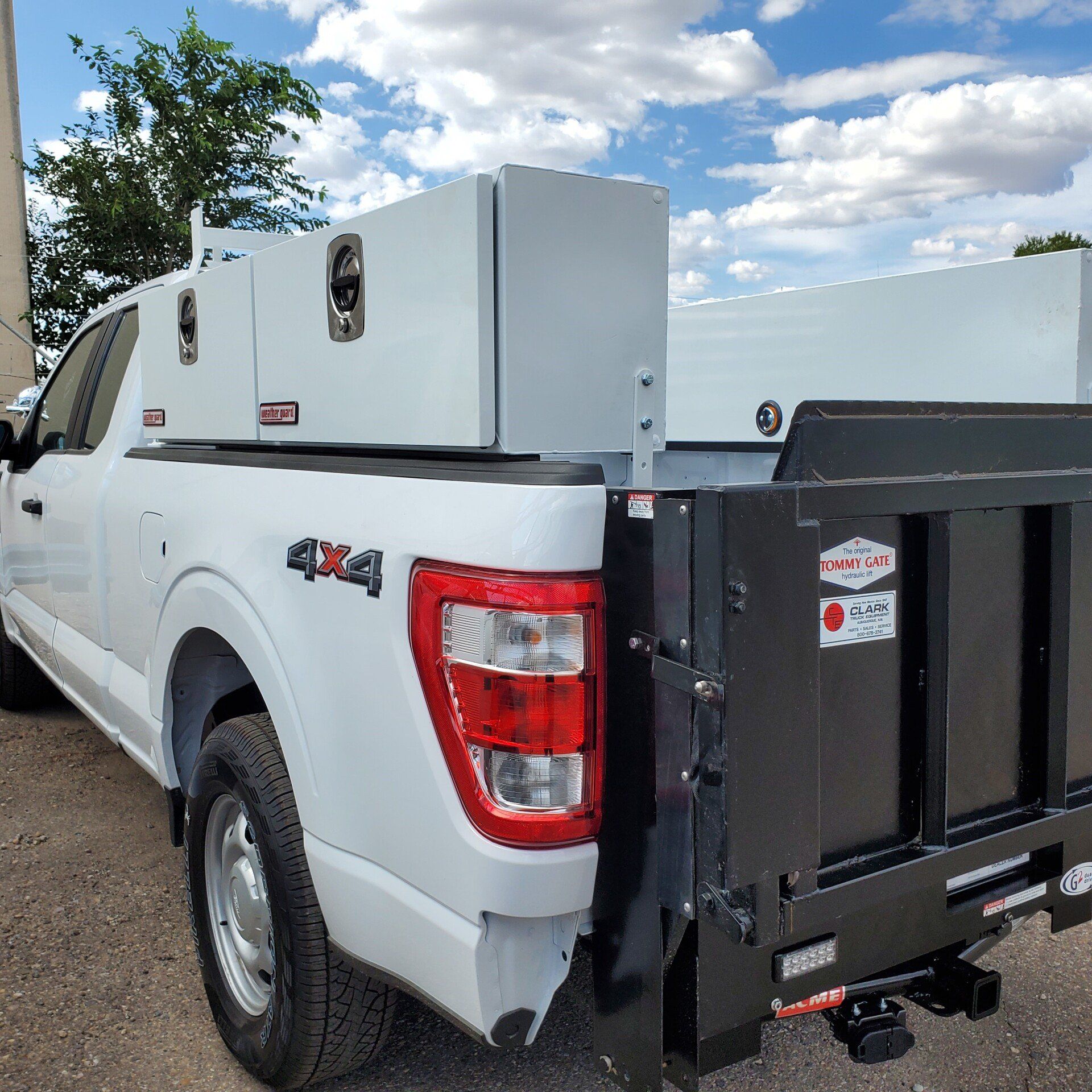 White pickup truck with a black dump bed and toolboxes, under a blue sky.