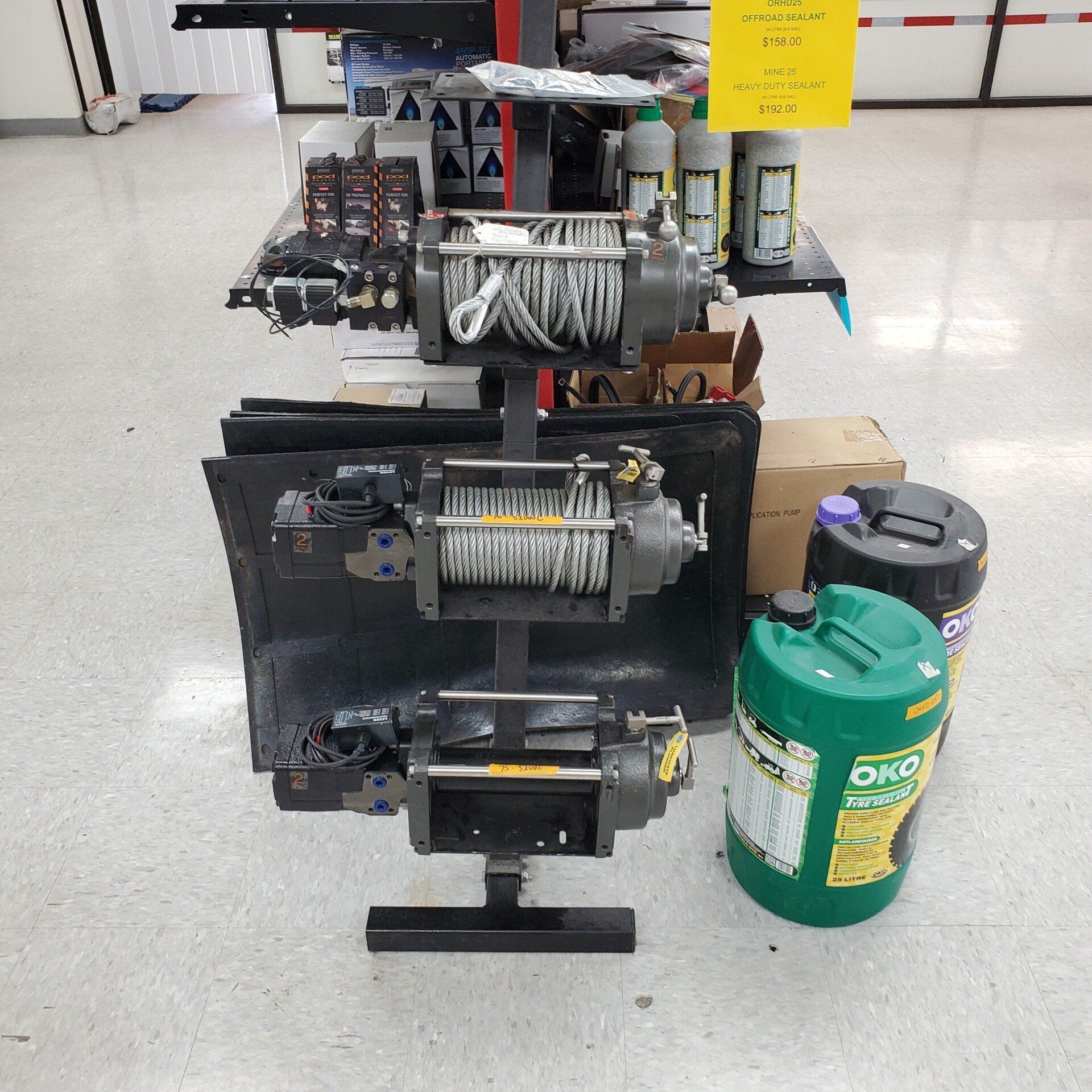 Three winches on display, black stand, with fluids and supplies in a store.