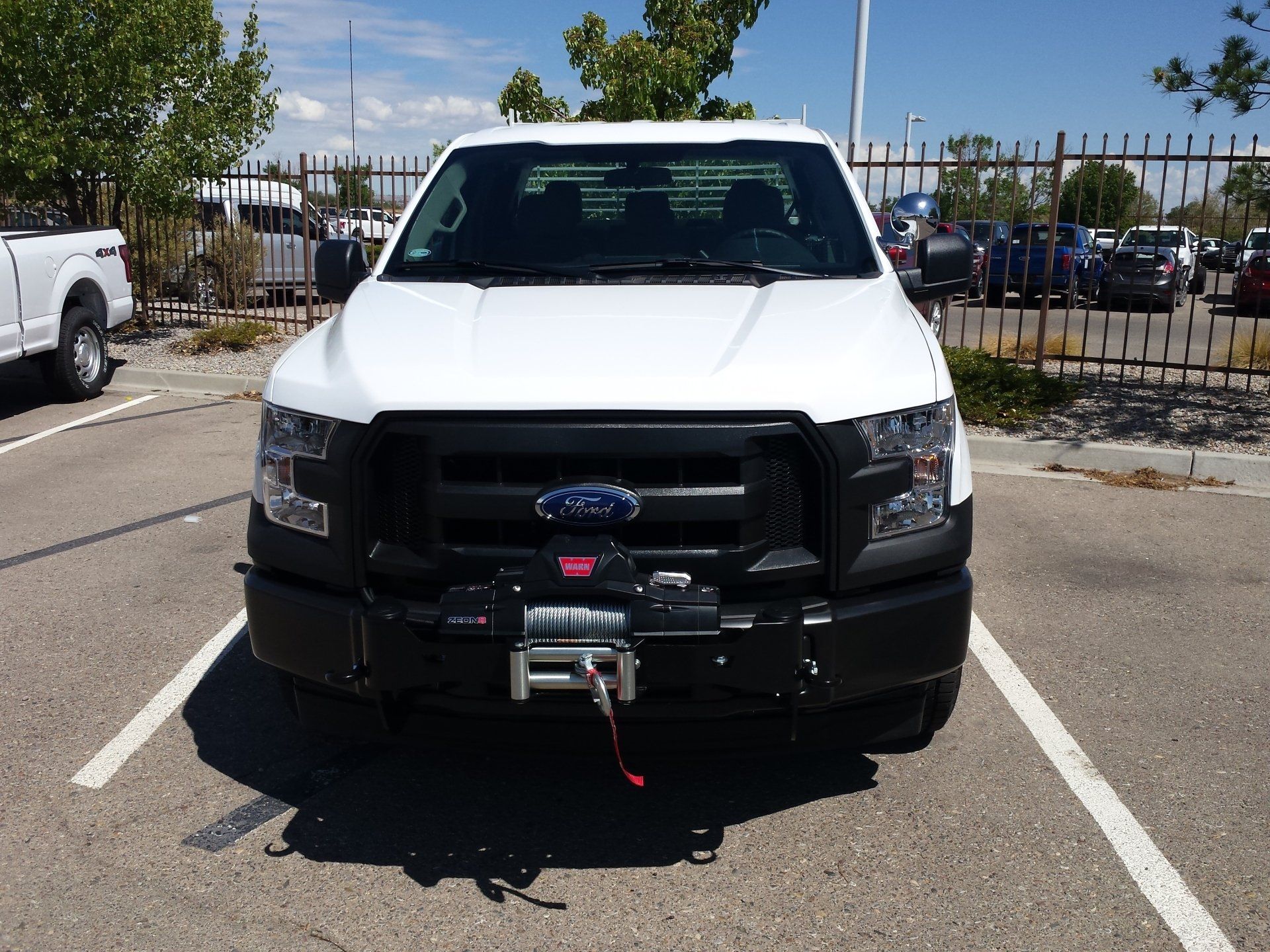 White Ford truck with black grill and winch, parked in a lot on a sunny day.