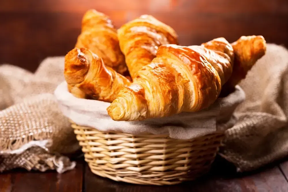 Basket of golden croissants on a rustic cloth and wooden table