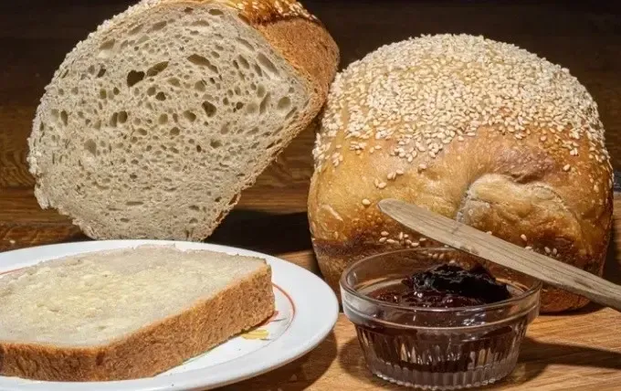Assorted rustic bread loaves and sliced bread with a small jar of jam on a wooden table