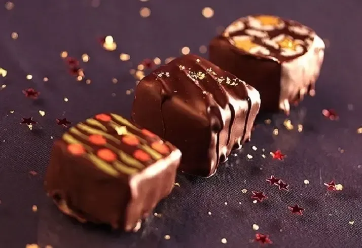 Three chocolate truffles with drizzled toppings on a dark surface with scattered sprinkles
