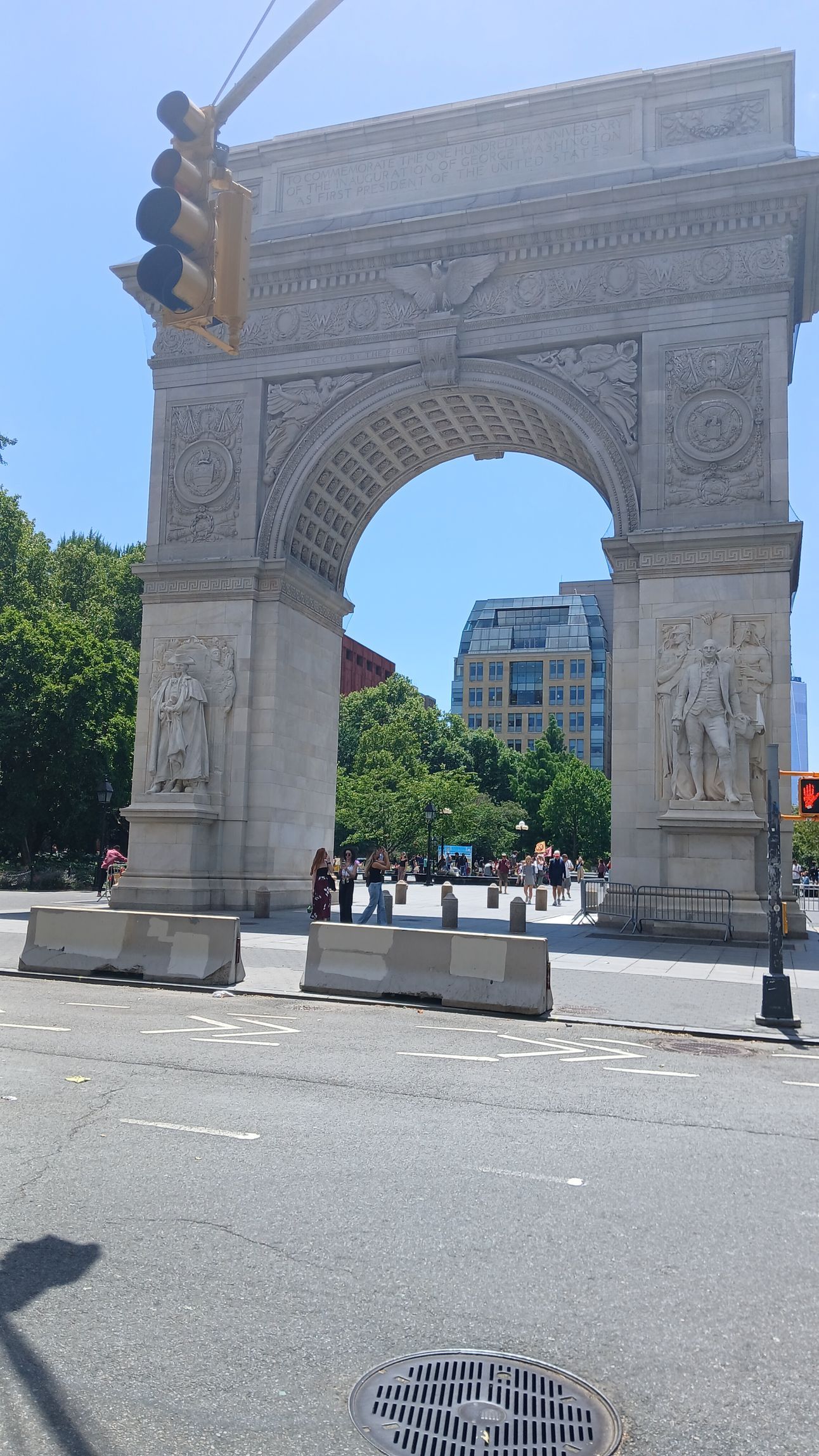 White ornate stone arch monument on a sunny street with pedestrians and buildings in the background