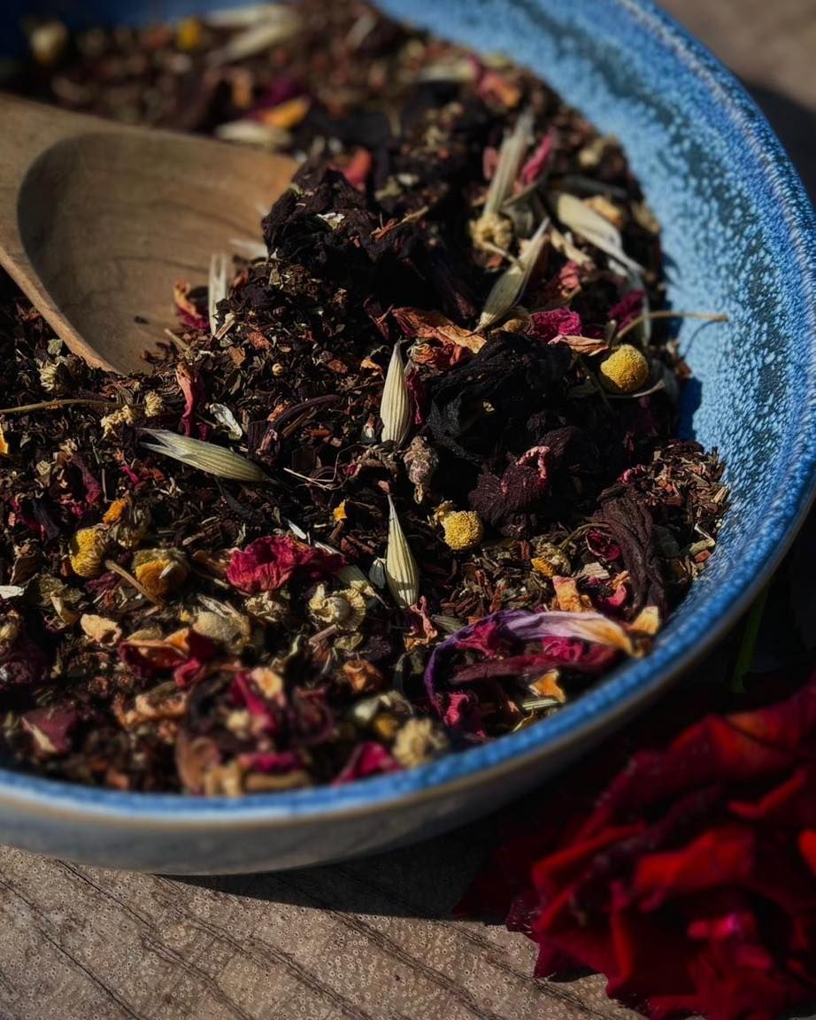 Loose dried tea leaves in a blue bowl with a wooden spoon, close-up.