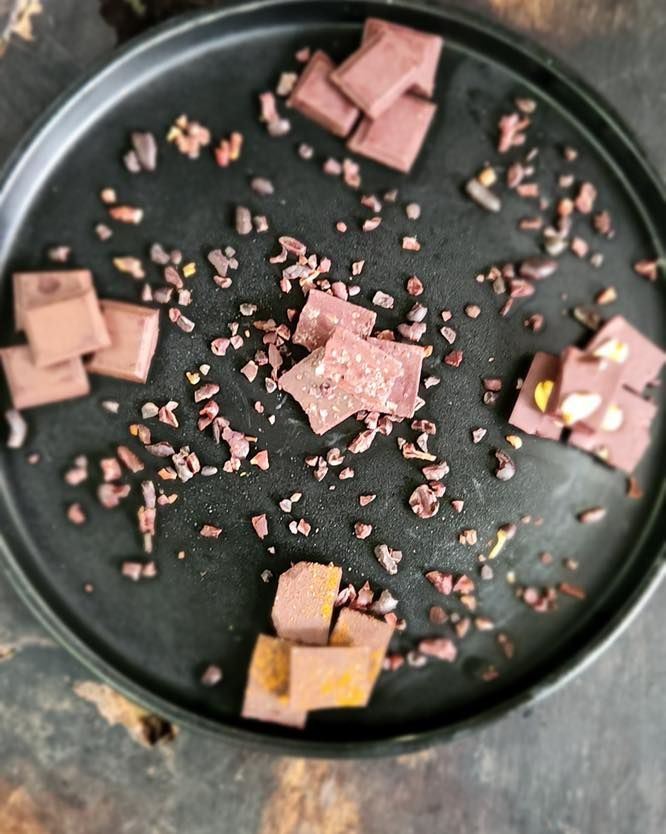 Scattered pink and yellow chocolate squares on a black plate with pink crumbs