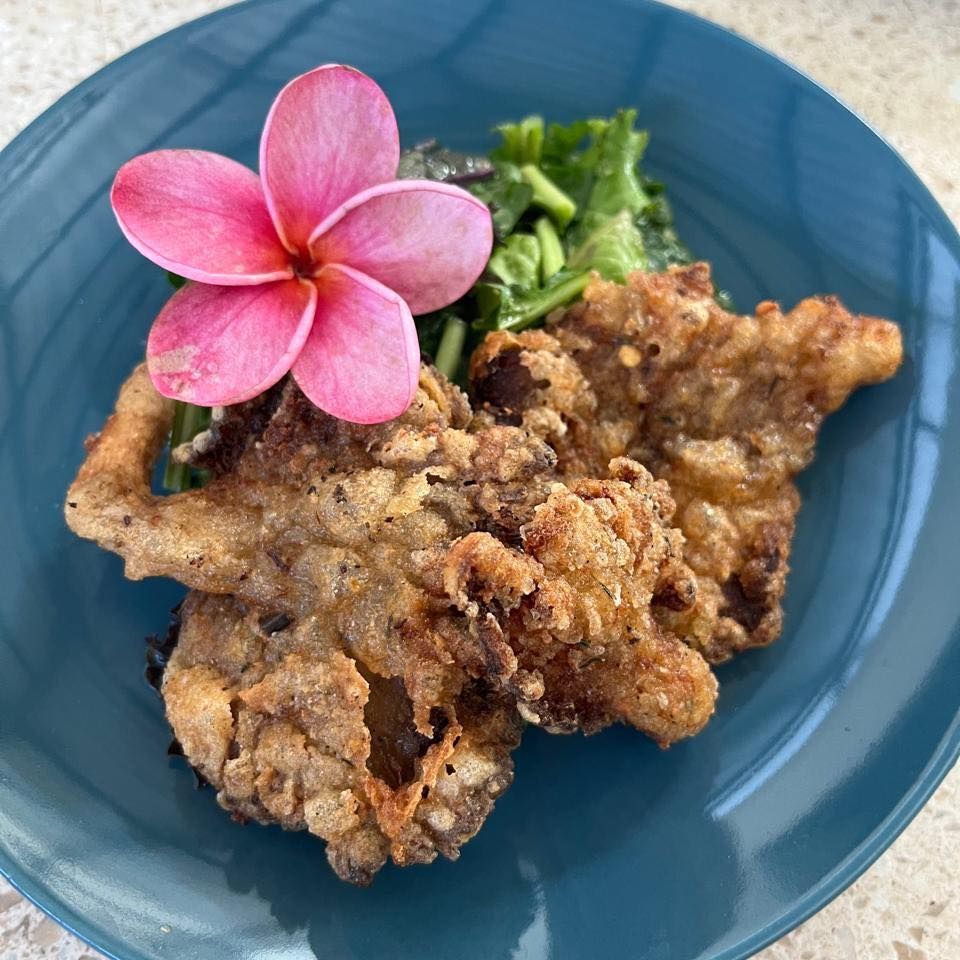 Fried chicken cutlet on a blue plate, garnished with a pink flower and greens