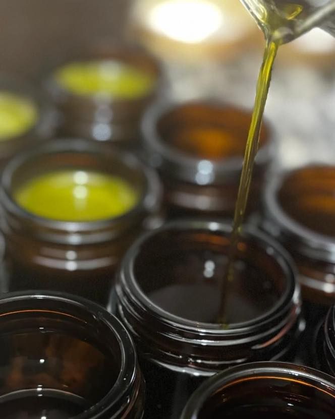 Oil being poured into small dark glass jars, with yellow-green liquid in the background.