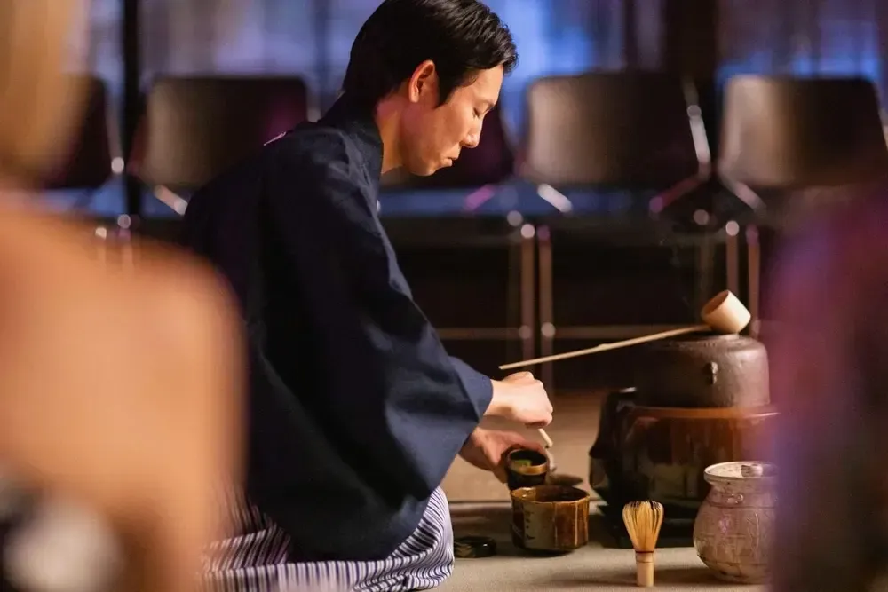 Person in dark clothing using a mallet at a wooden drum in a dim performance setting