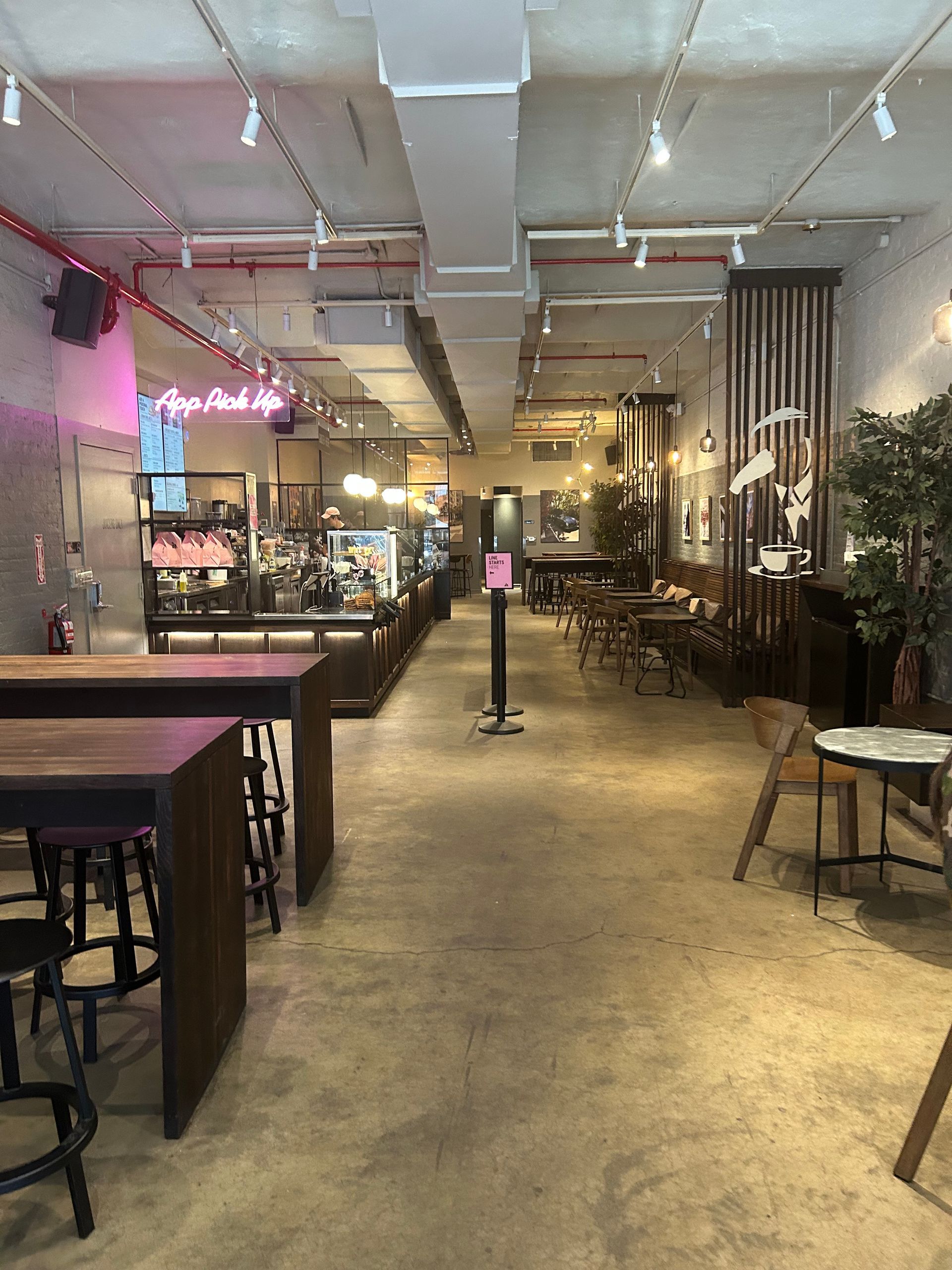 Empty modern cafe interior with high tables, stools, plants, and exposed ceiling pipes