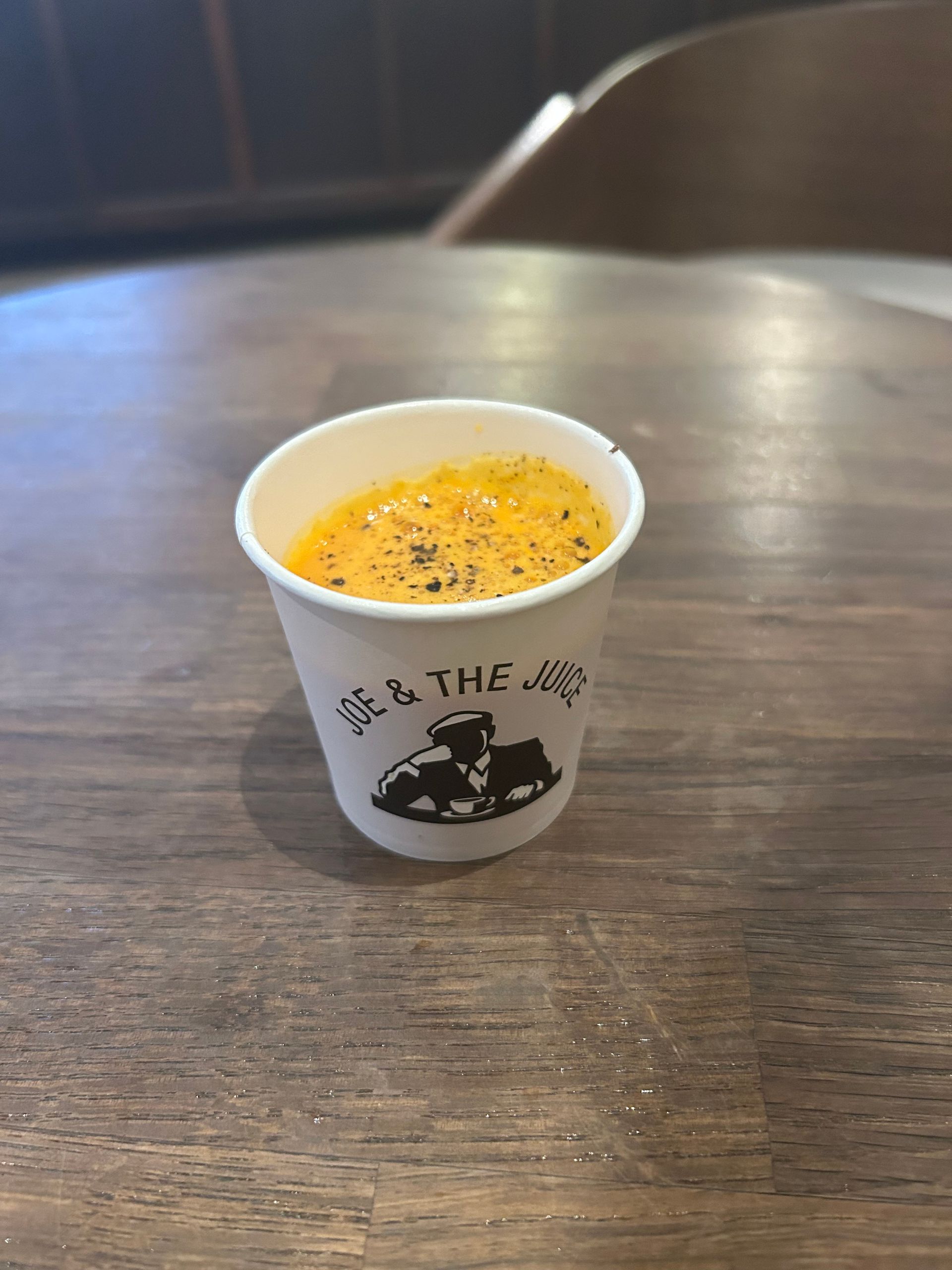 Small paper cup of orange dessert topped with spices on a wooden table