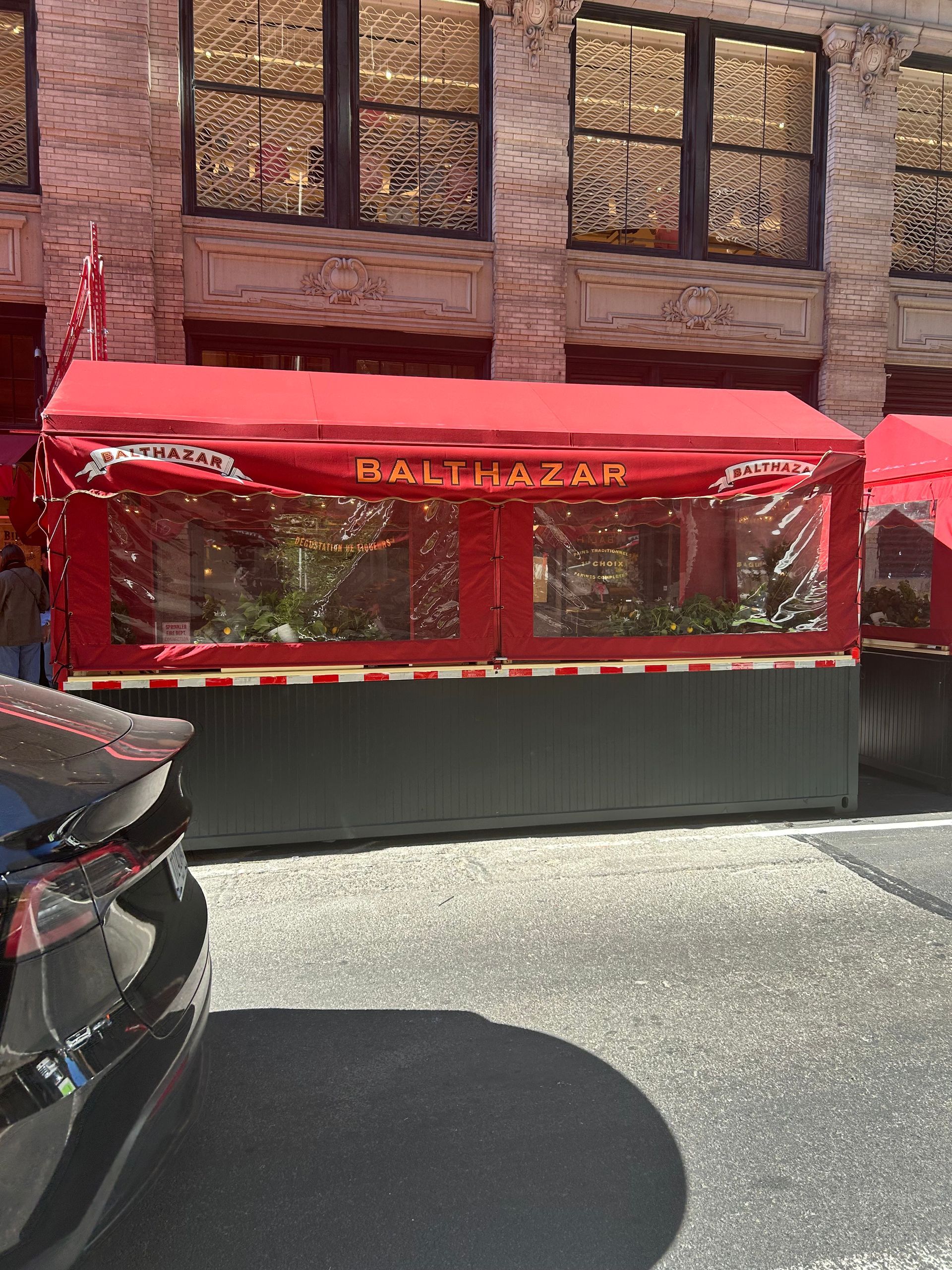 Red patio awning over a fenced outdoor dining area beside a brick building.