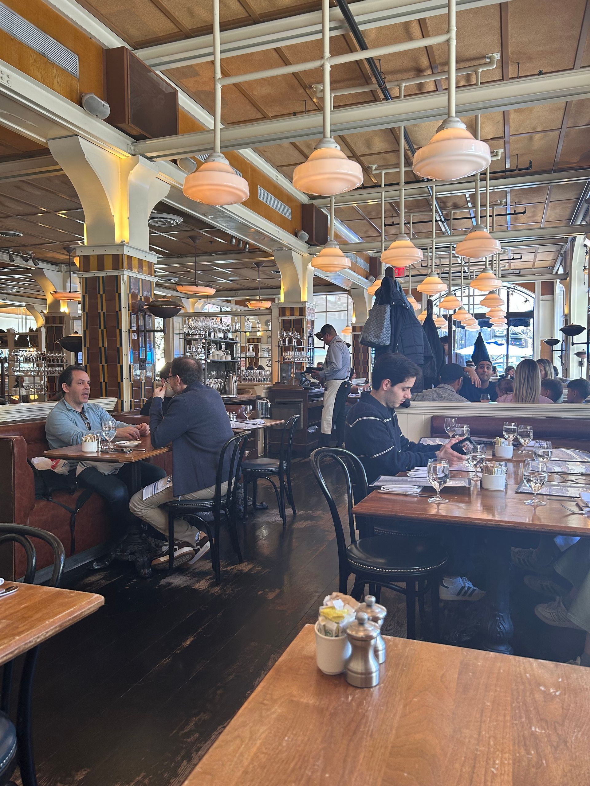 Busy restaurant interior with diners at tables and warm hanging lights under a high wooden ceiling