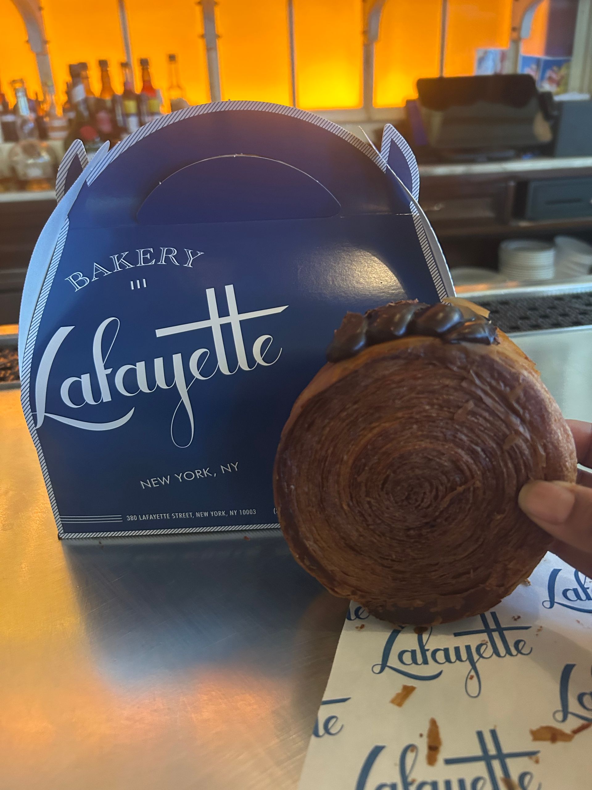 Chocolate croissant held in front of a blue Lafayette bakery bag and napkin on a counter