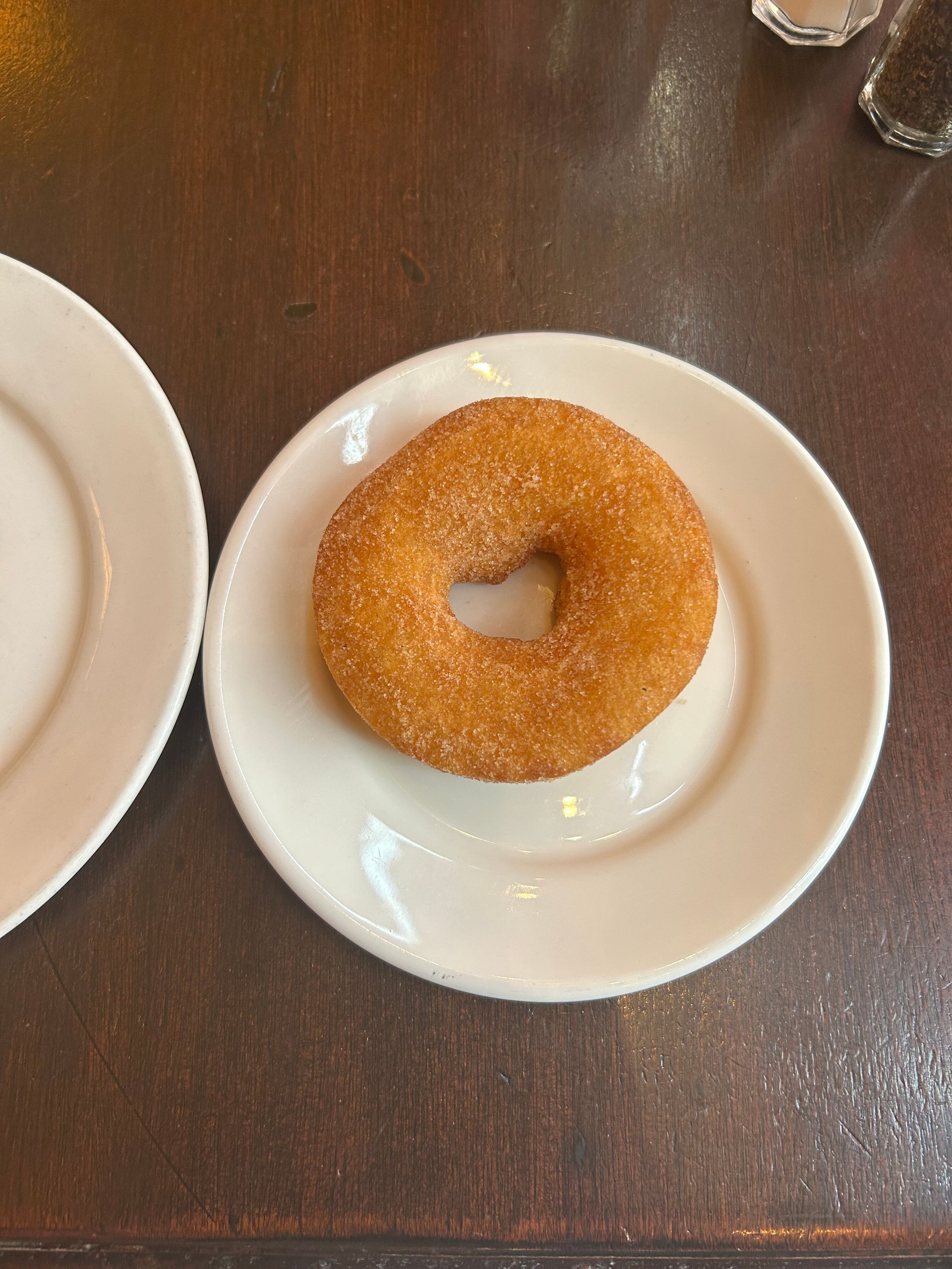 Plain donut on a white plate on a wooden table, with part of another plate visible beside it