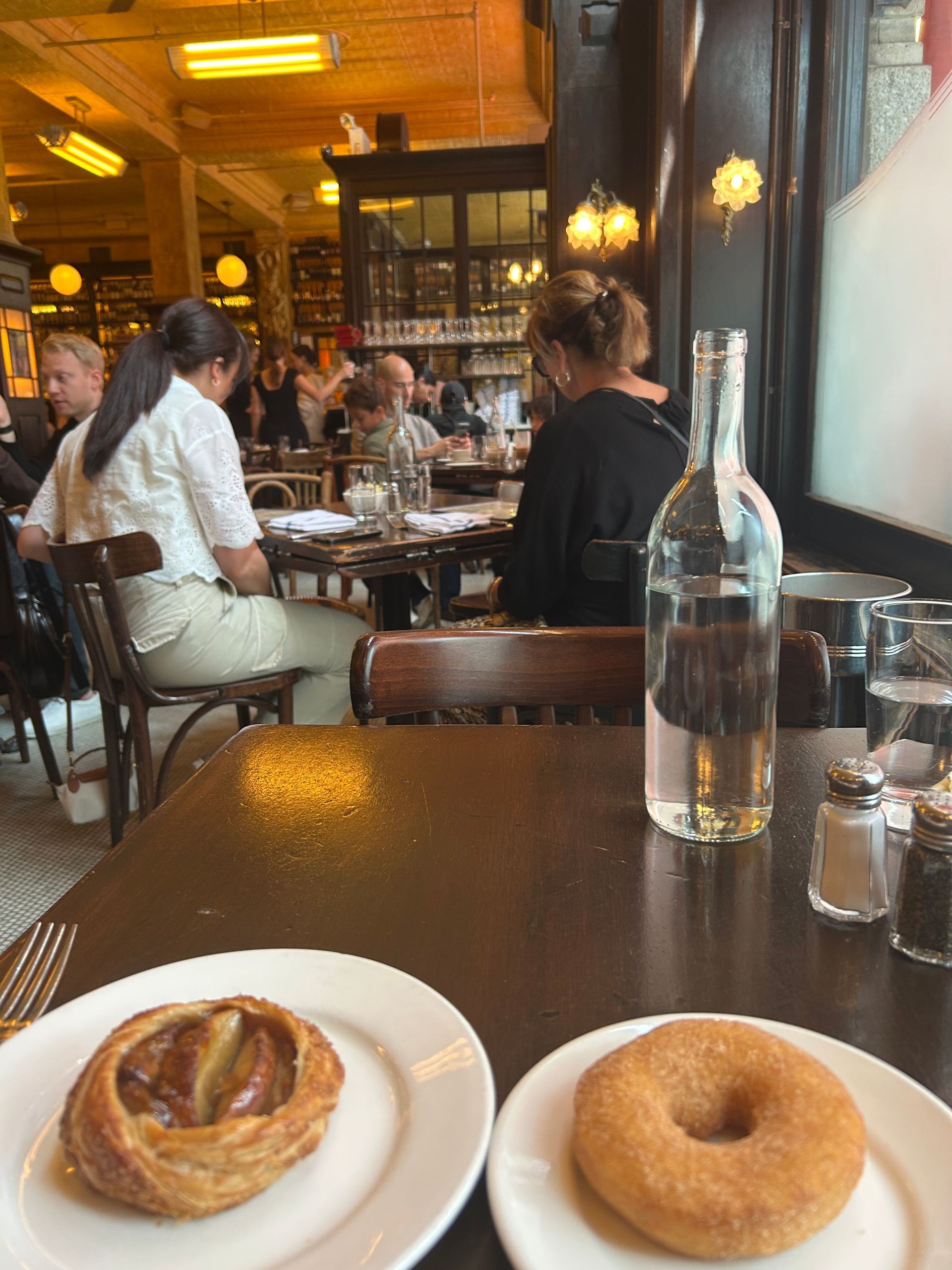 Cafe table with a pastry, donut, and water bottle in a warm, busy restaurant interior