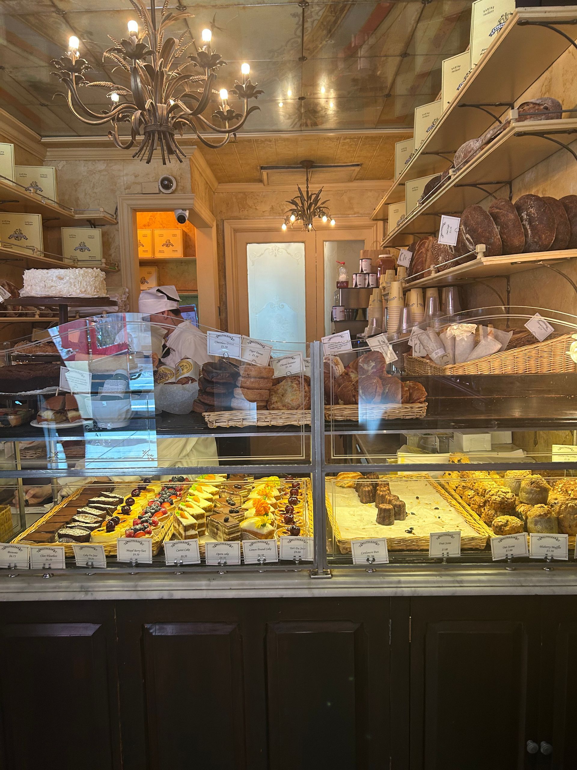Bakery display case with assorted pastries and cakes in a warm, mirrored shop interior