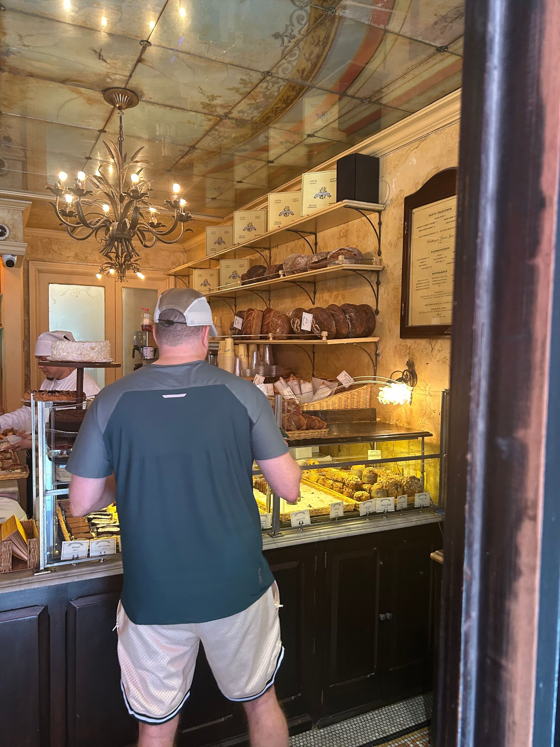 Person browsing a display case in a cozy shop with chandeliers and shelves of goods.