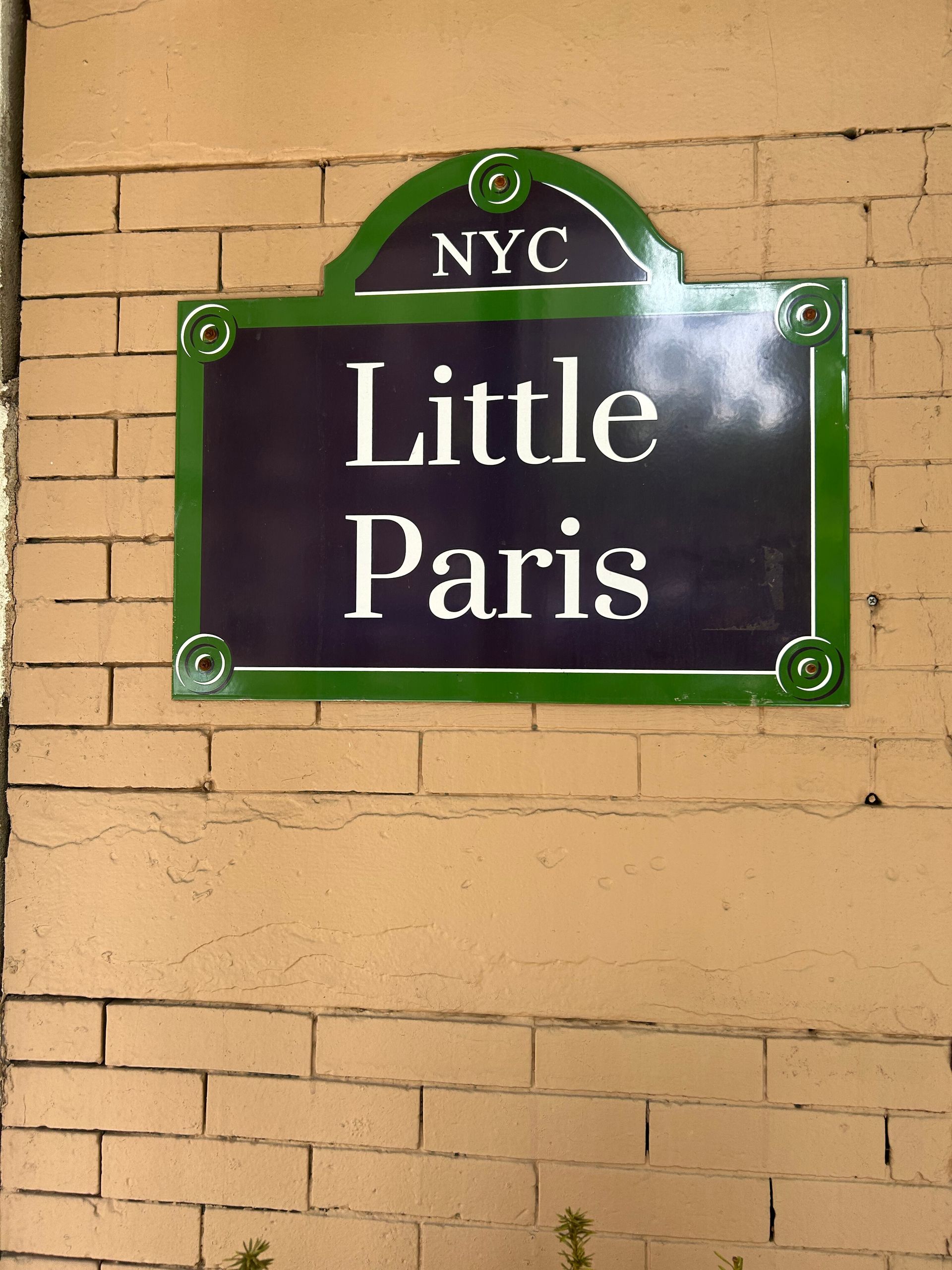 NYC “Little Paris” street sign mounted on a beige brick wall