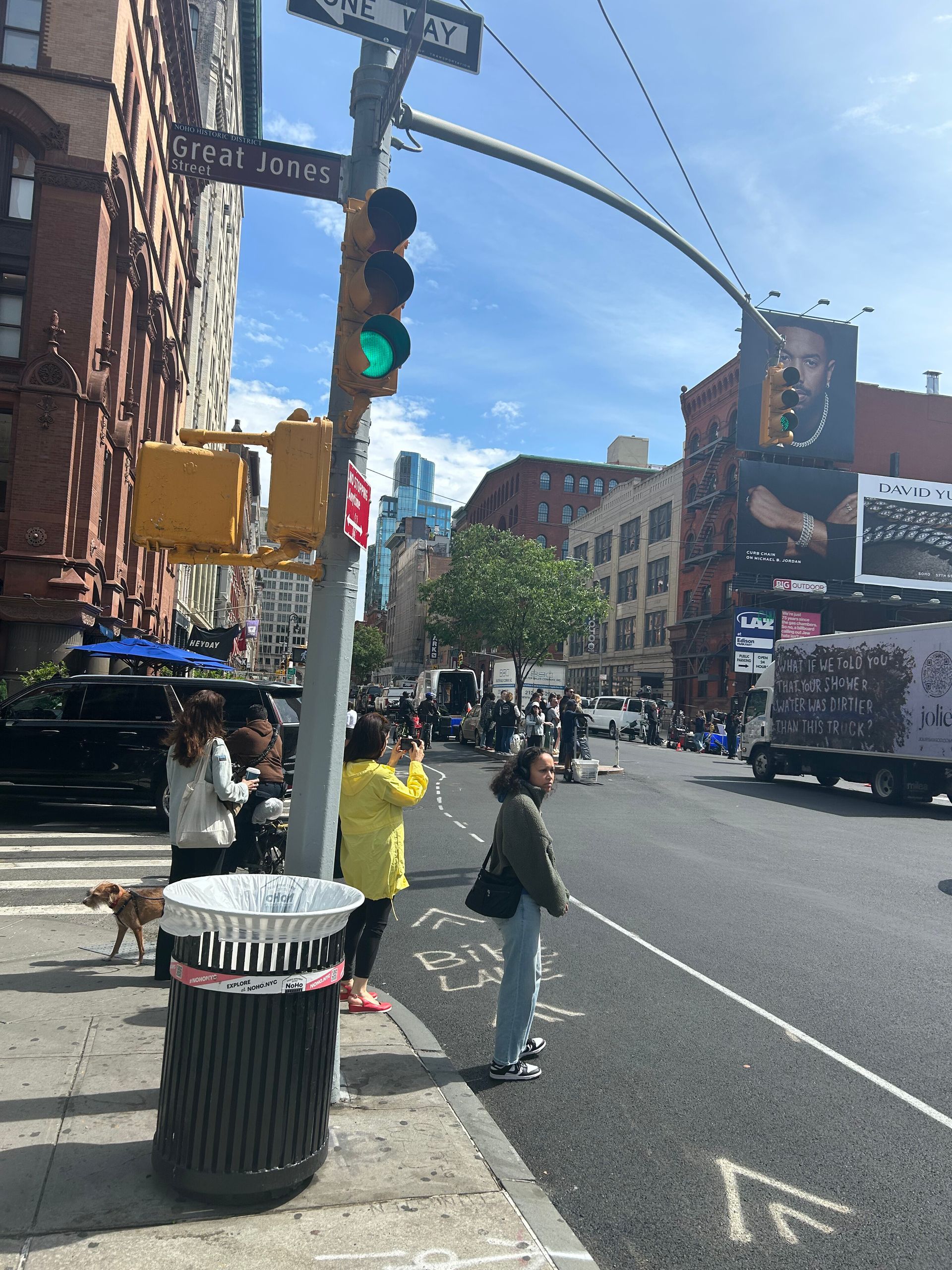 City street corner with pedestrians, traffic light, trash can, and buildings on a sunny day