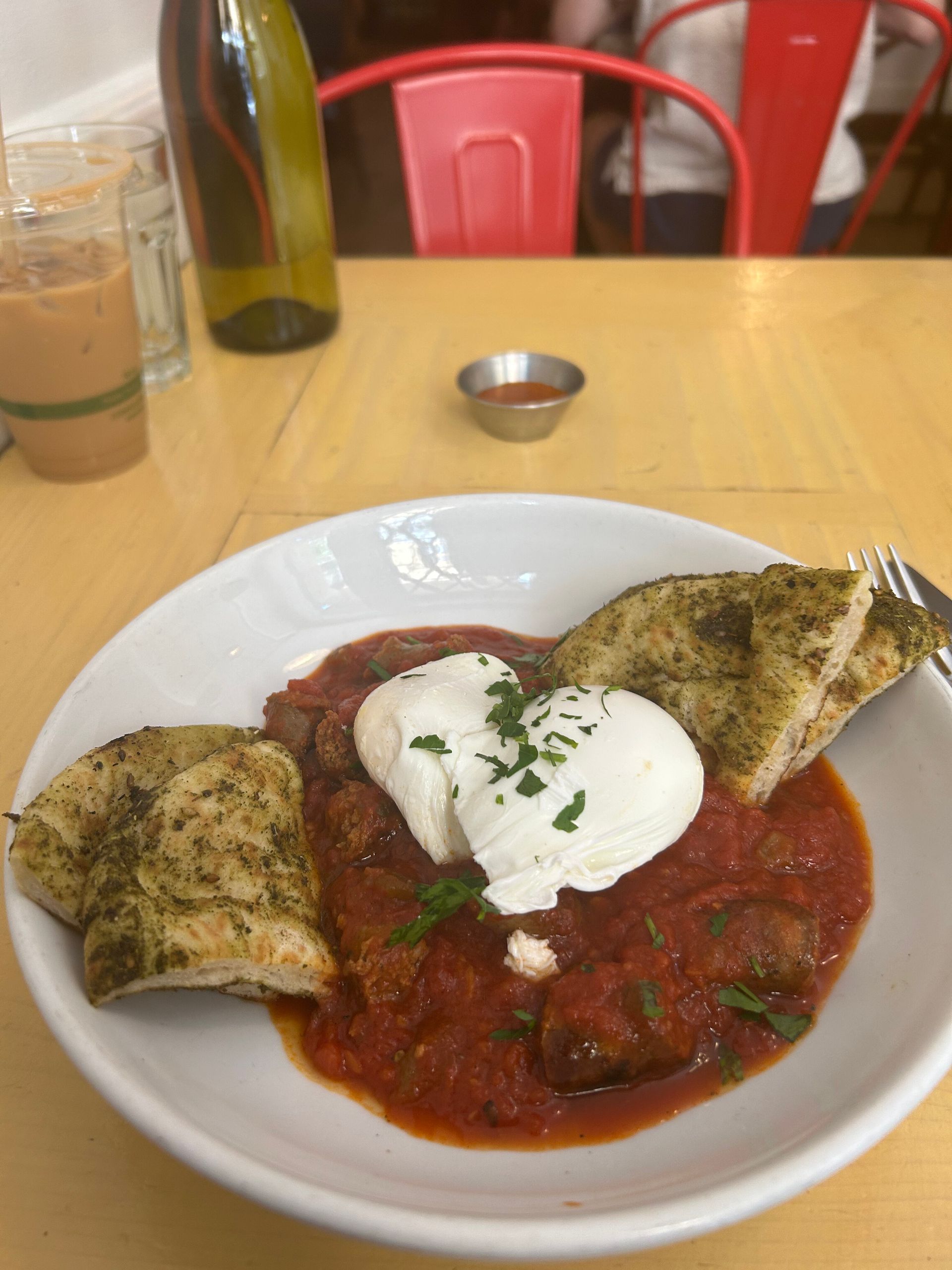 Plate of red saucy food topped with white cream on a restaurant table with bread on the side