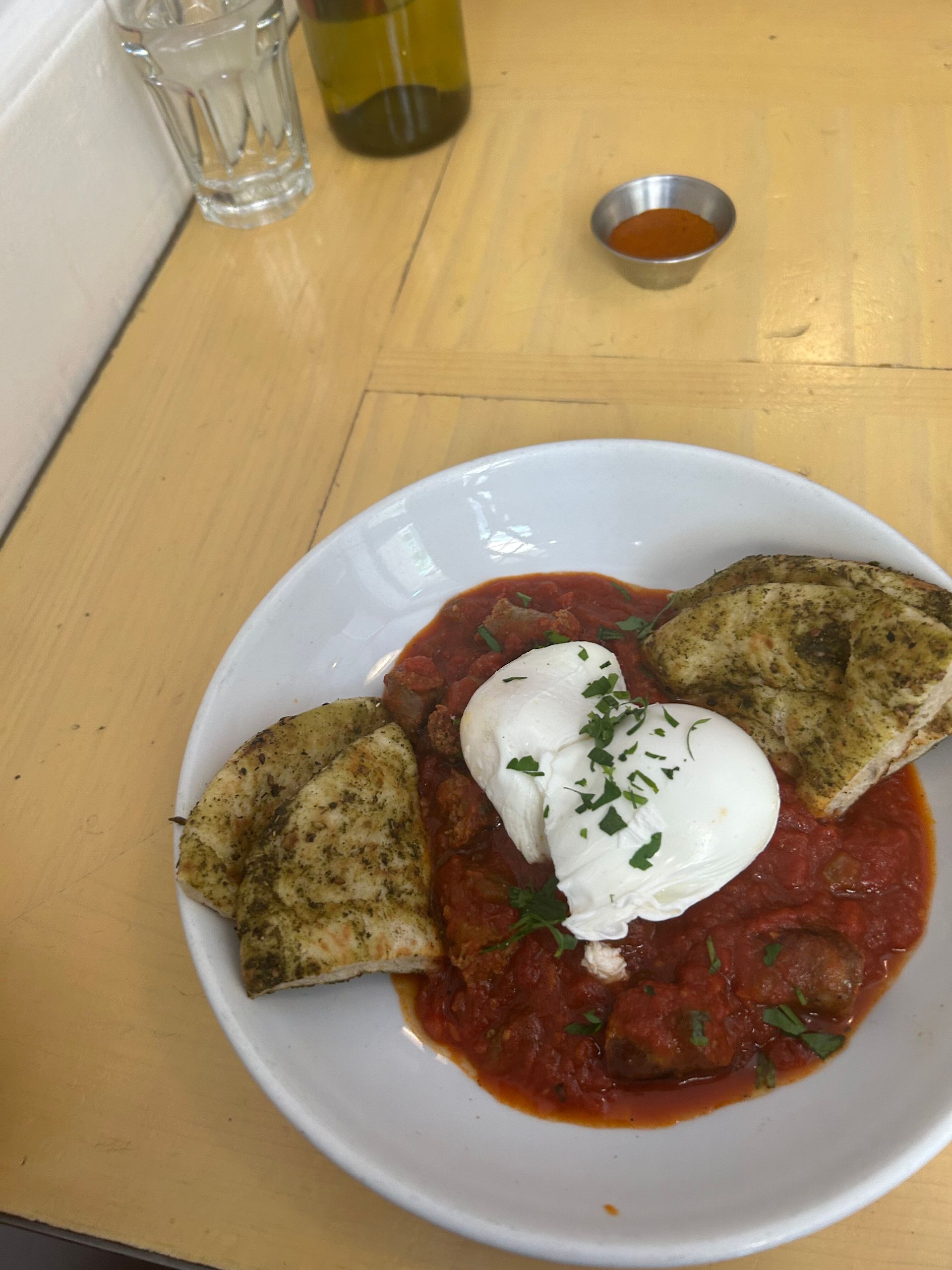 Plate of tomato pasta with white cheese and herbs on a wooden table, with bread on the side.