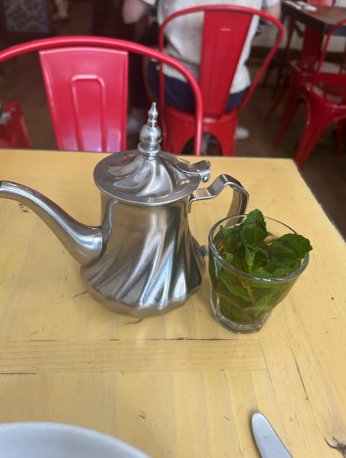 Silver teapot and mint tea glass on a wooden table with red chairs in the background