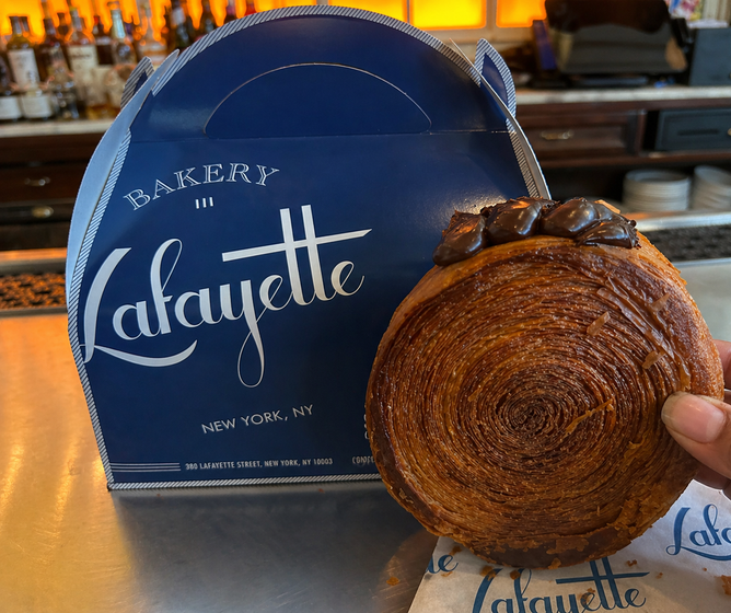 Brown pastry held in front of a blue Lafayette Bakery box on a counter.
