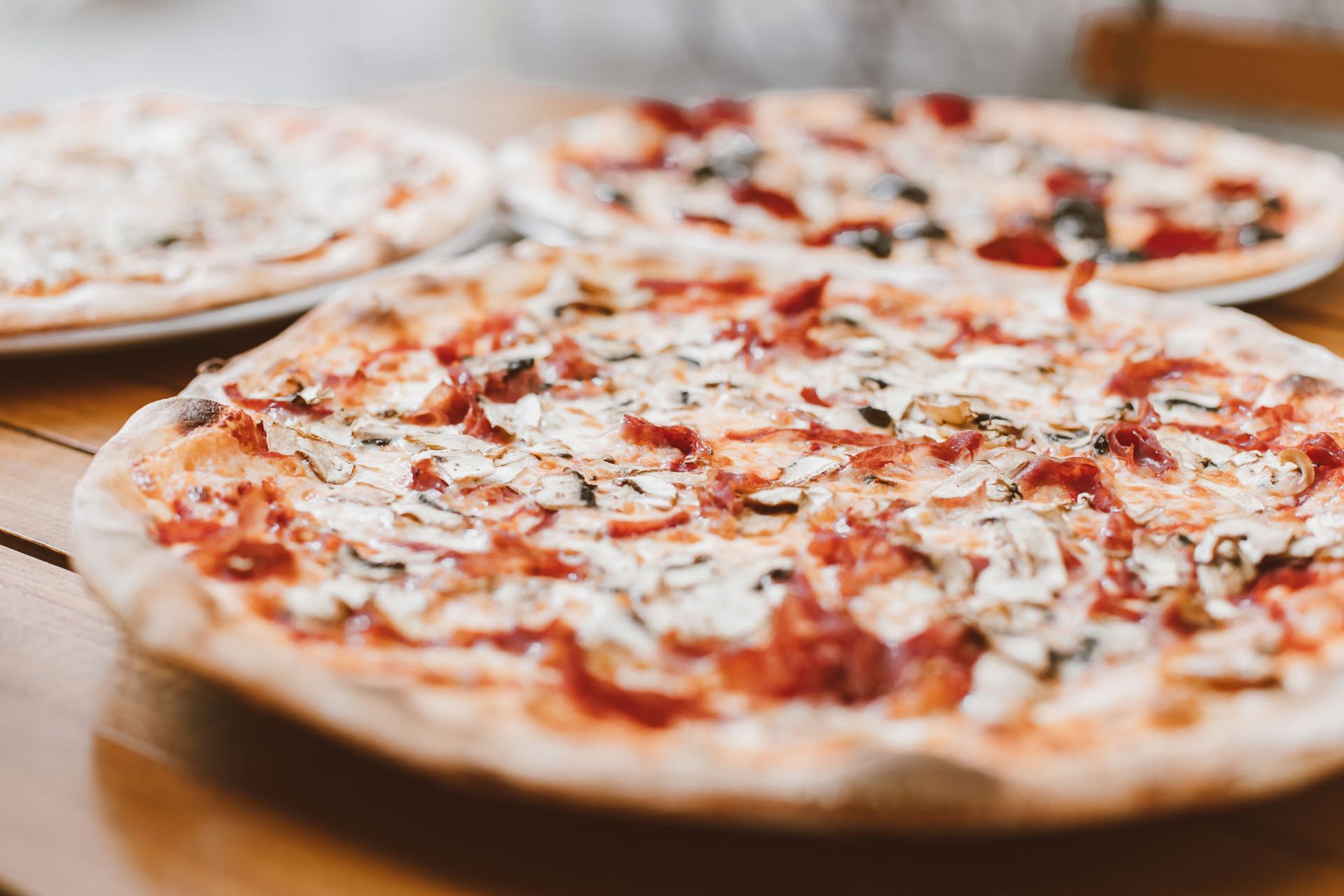 Three pizzas on wooden tables, topped with tomato sauce, cheese, and herbs