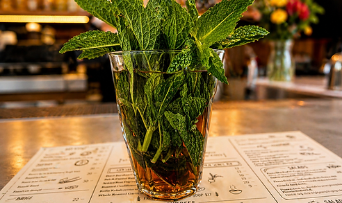 A glass of mint leaves in a cocktail at a bar, on top of a menu.