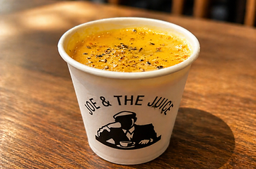 Coffee cup of soup or latte with pepper on top, on a wooden table at Joe & The Juice