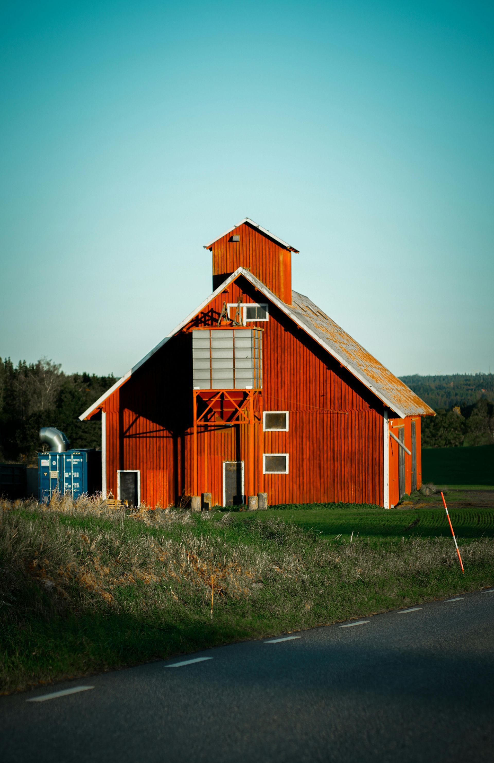 Red barn with a small cupola beside a road under a clear blue sky.