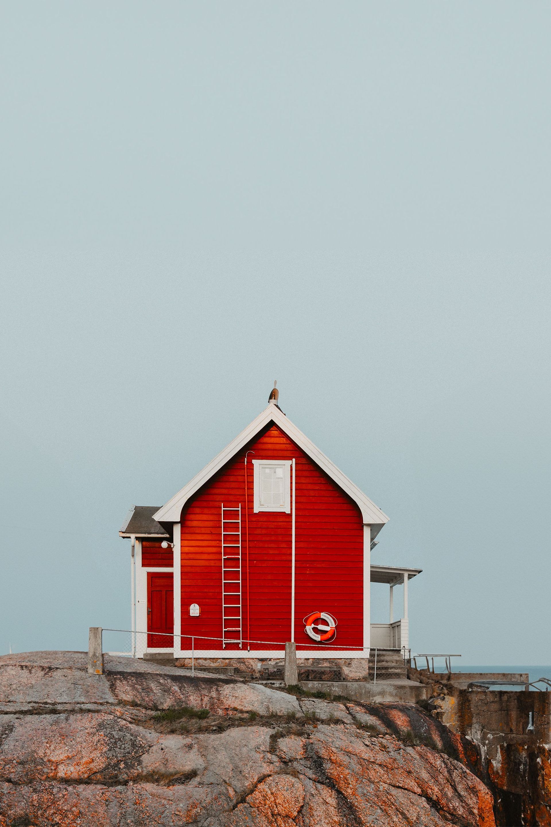 Red seaside hut on rocky shore beneath a pale sky